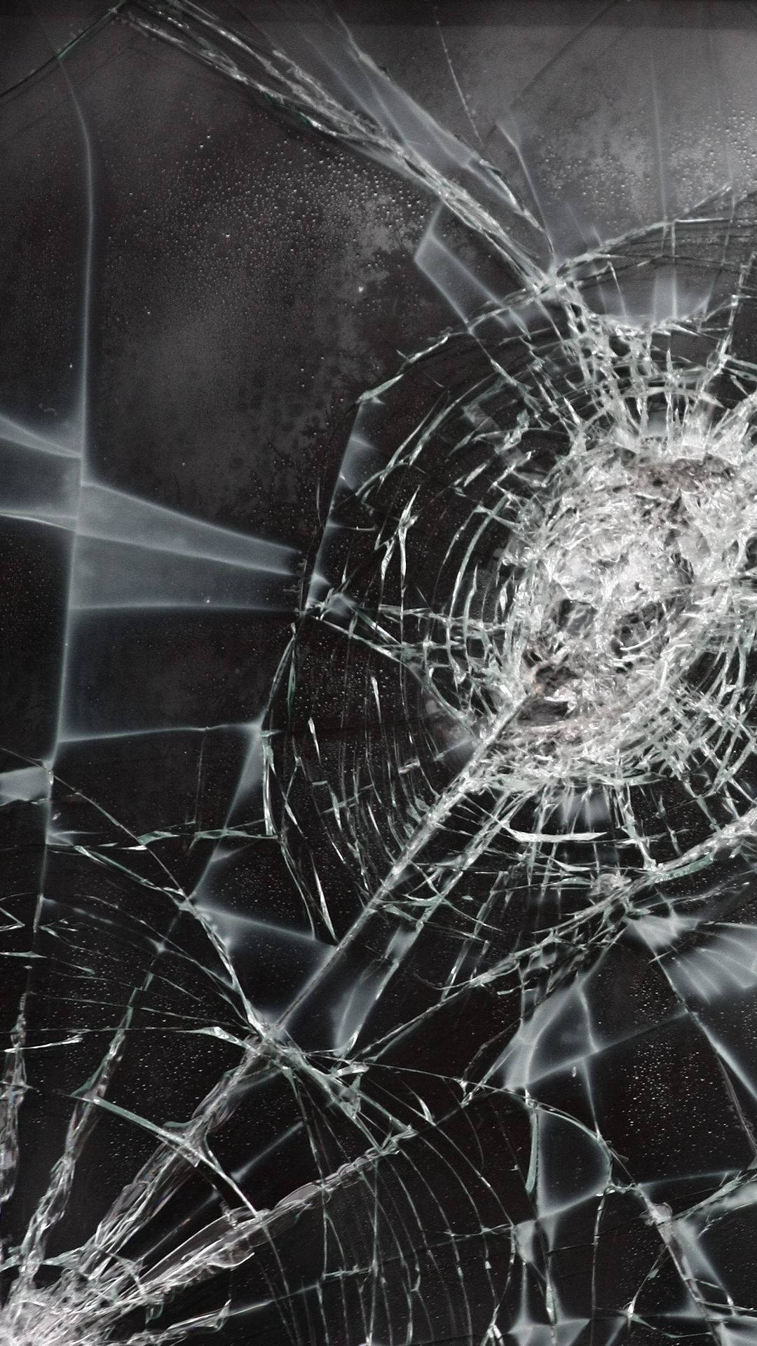 cracked 桌布 壁紙 — 一塊破碎的玻璃表面，從中央撞擊點放射出複雜的裂紋，背景為深色。