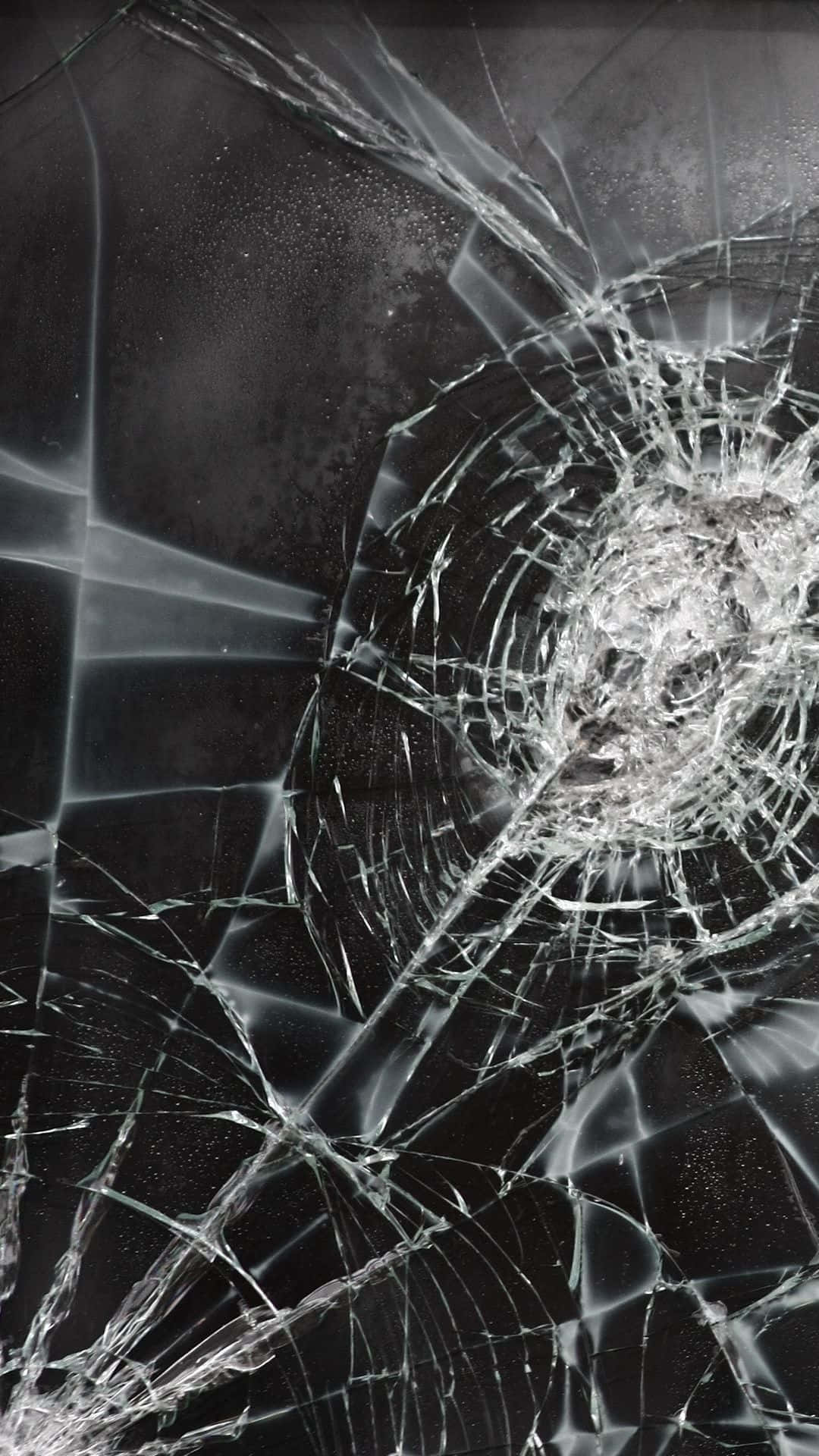 iPhone 桌布 壁紙 — 一塊破碎的玻璃表面，從中央撞擊點向外輻射出複雜的裂紋，背景為深色。
