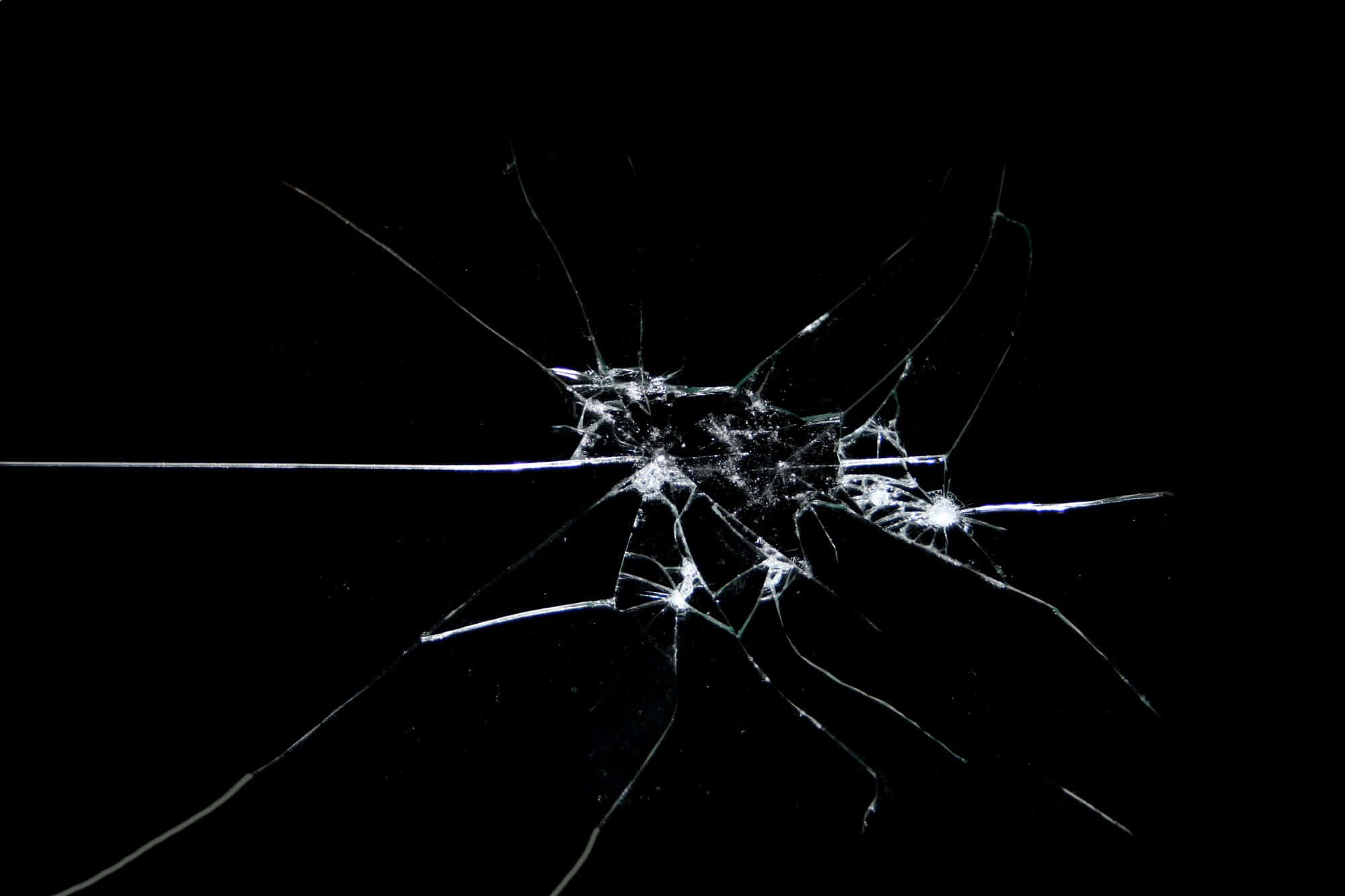 Fracture Glass 桌布 壁紙 — 一塊破碎的玻璃表面，從中央撞擊點散發出複雜的裂紋，背景為純黑色。