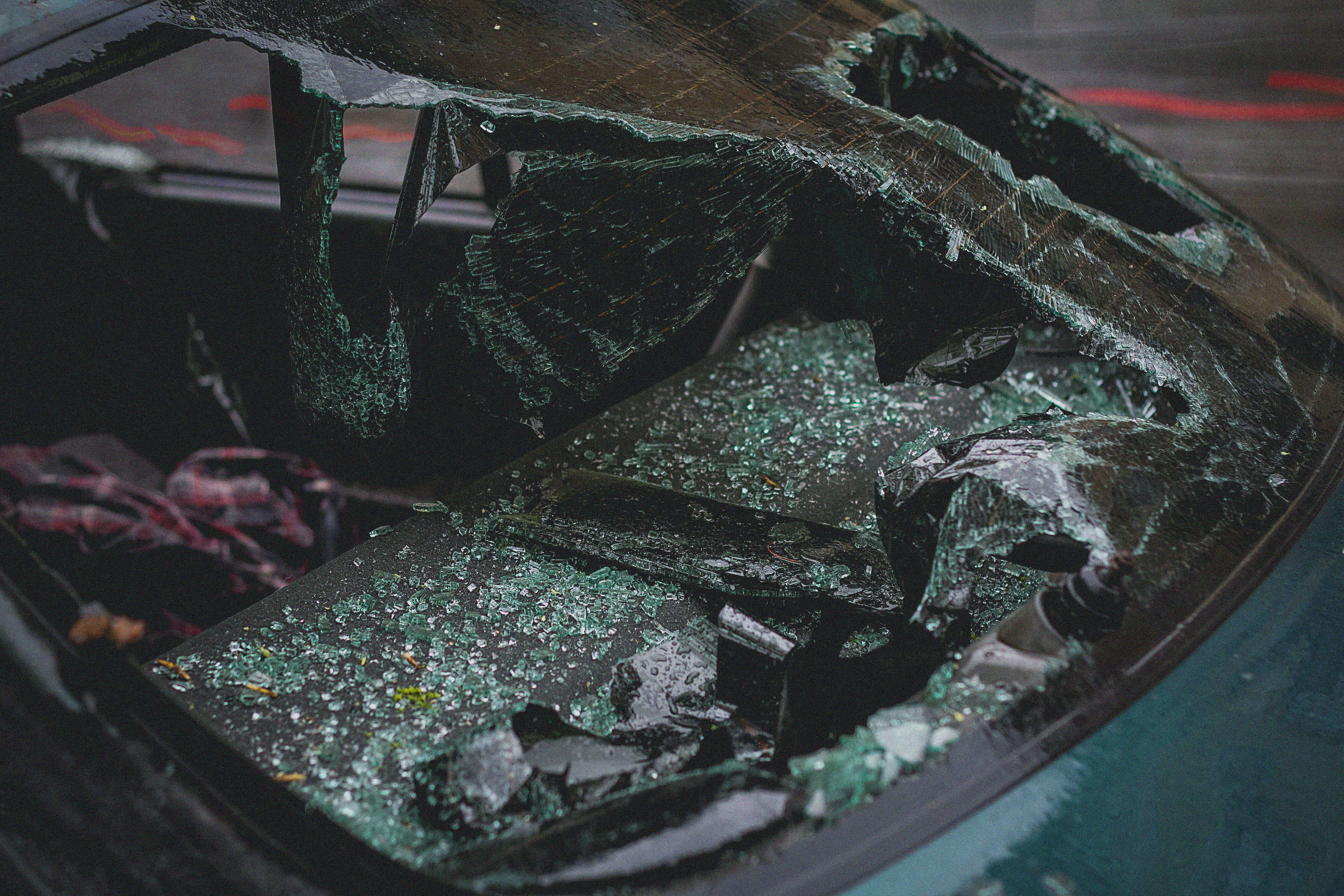 car crash 桌布 壁紙 — 一塊碎裂的汽車擋風玻璃，帶有綠色玻璃碎片，雨滴附著在破碎的表面上。