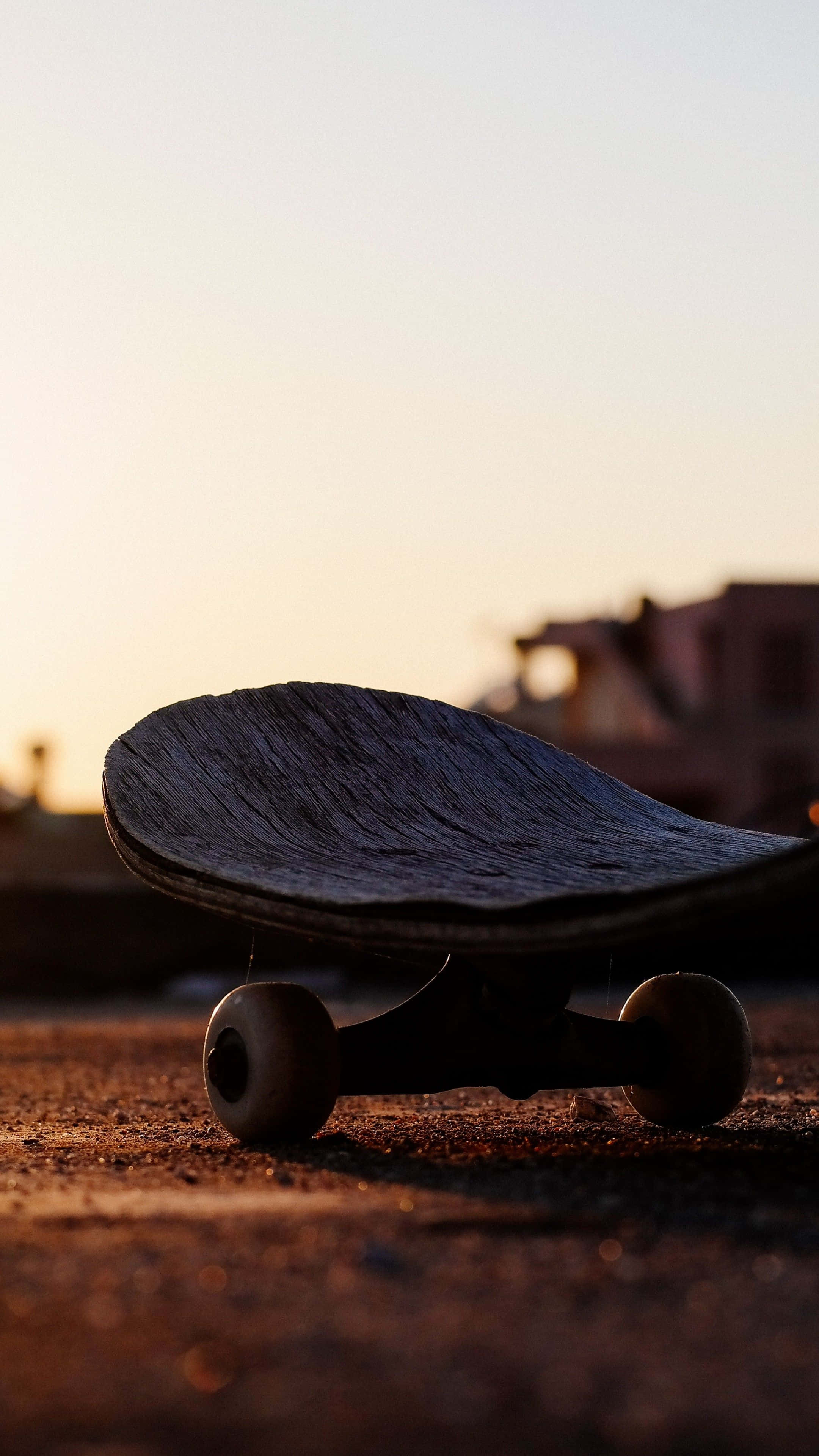 skateboarding 桌布 壁紙 — 一塊磨損的滑板放在粗糙的路面上，沐浴在溫暖的金色夕陽光中，背景是模糊的城市建築。