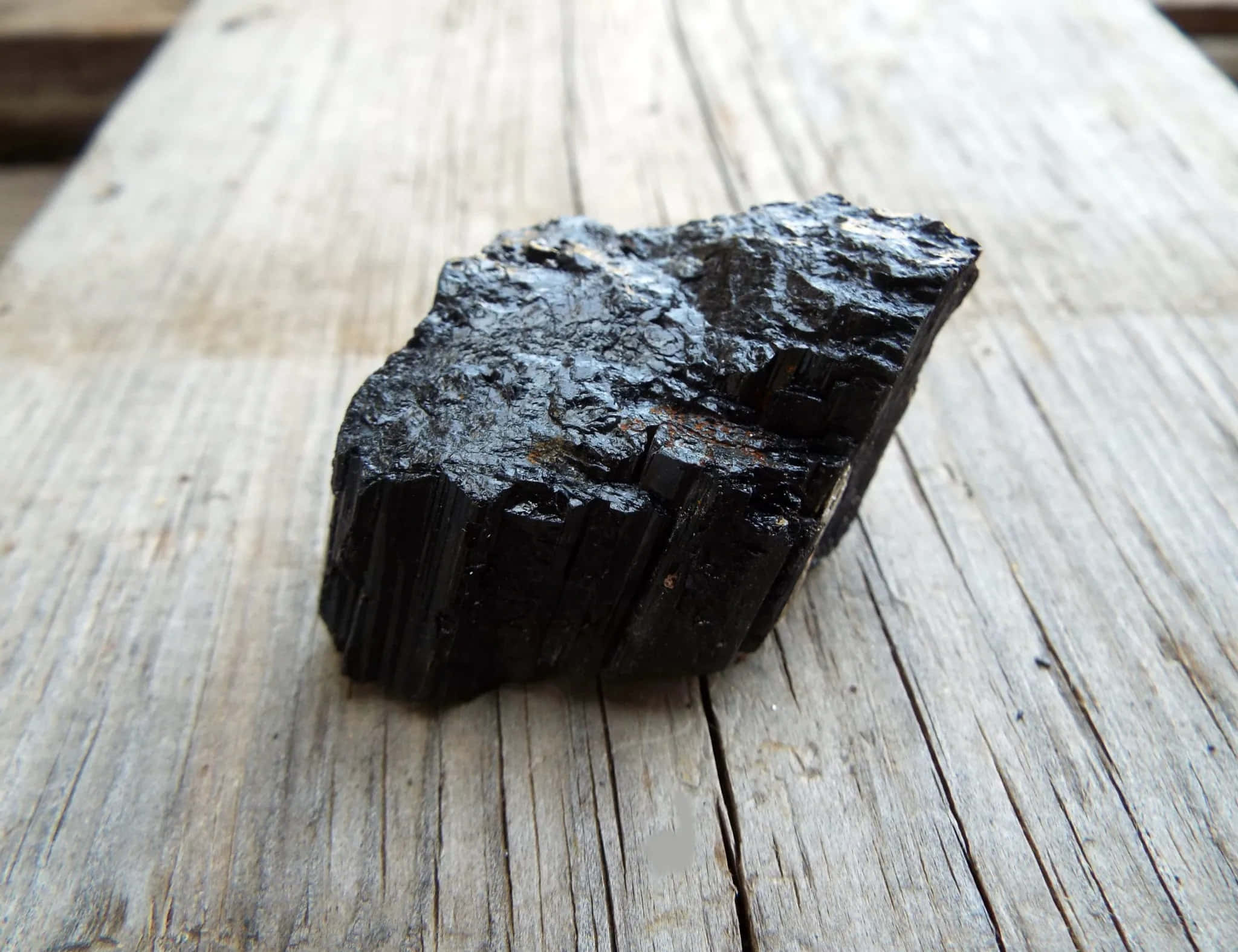 Dark Rock 桌布 壁紙 — 一塊粗糙的黑色礦物標本，帶有光澤的晶面，放置在風化的木質表面上。