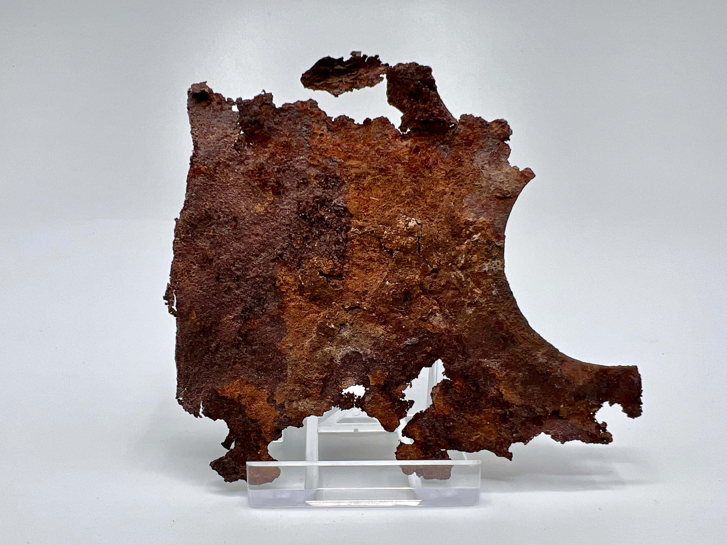 Museum 桌布 壁紙 — 一塊經風化、邊緣參差不齊的生鏽金屬碎片，放置在透明壓克力支架上，背景為純白色。