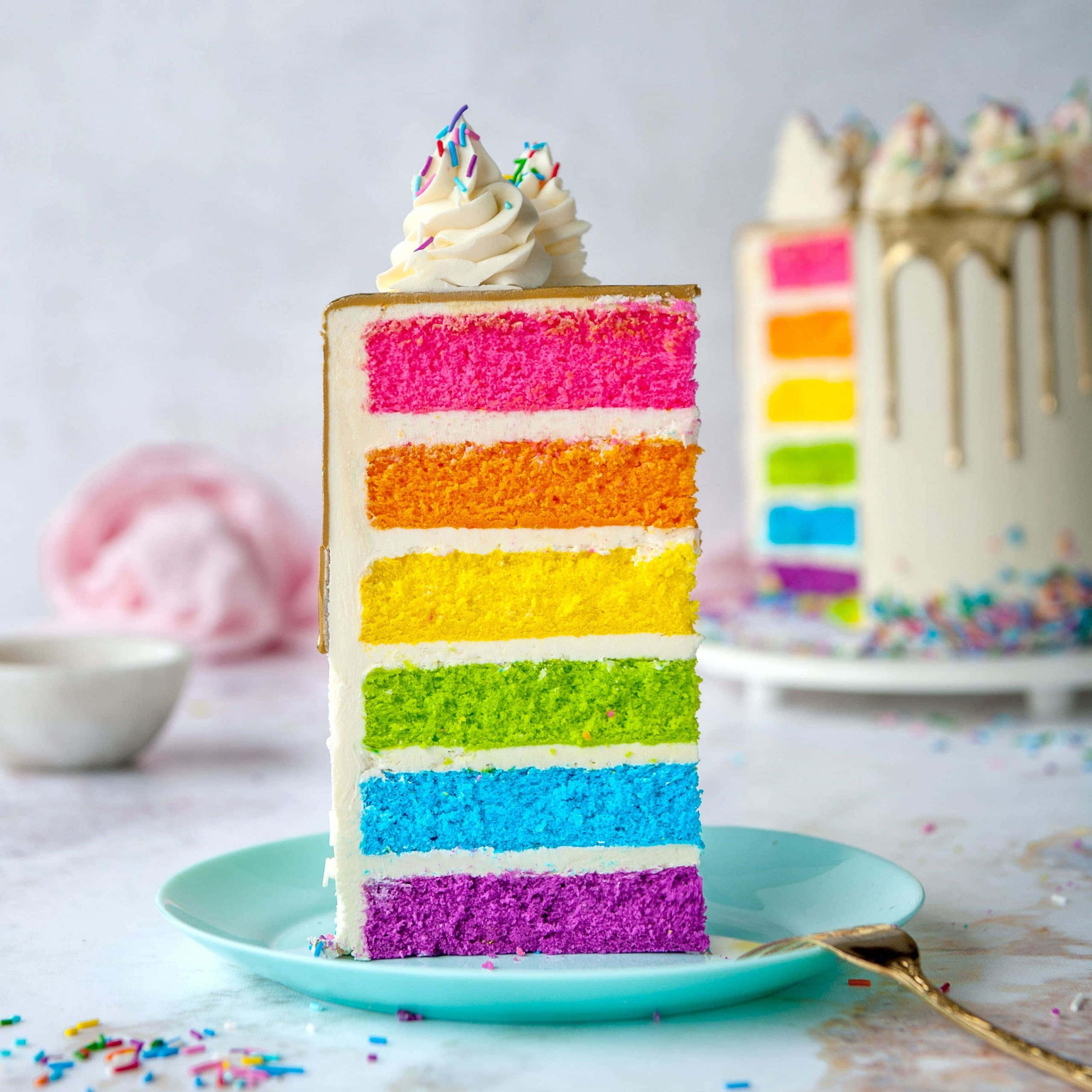 Birthday Cake 桌布 壁紙 — 一塊色彩繽紛的彩虹千層蛋糕，上面灑滿彩色糖粒，放在青綠色盤子上，背景是柔和的白色。