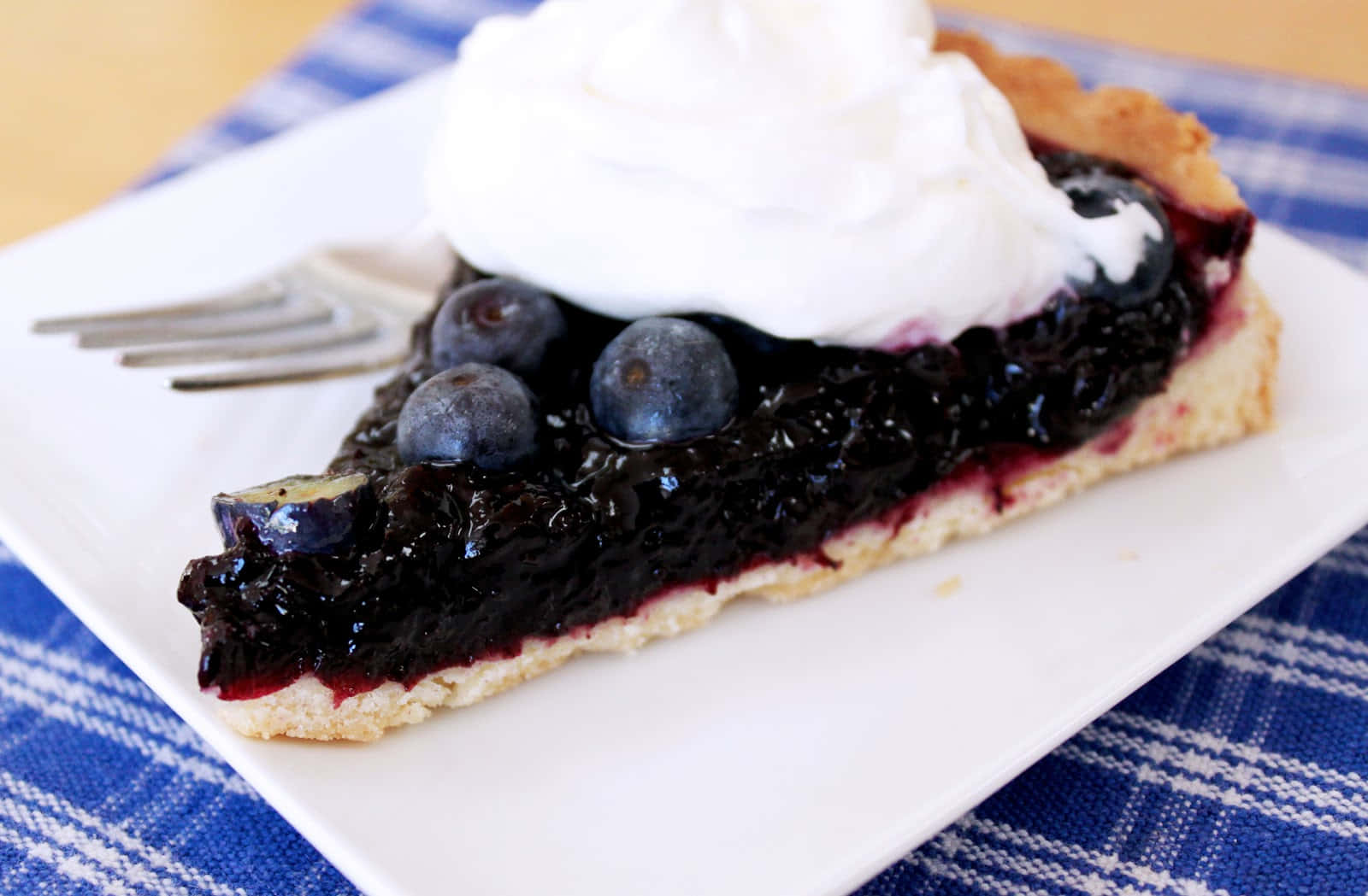 Blueberries Tart 桌布 壁紙 — 一塊藍莓派加上鮮奶油，放在白色盤子上，盤下是藍色格紋布。