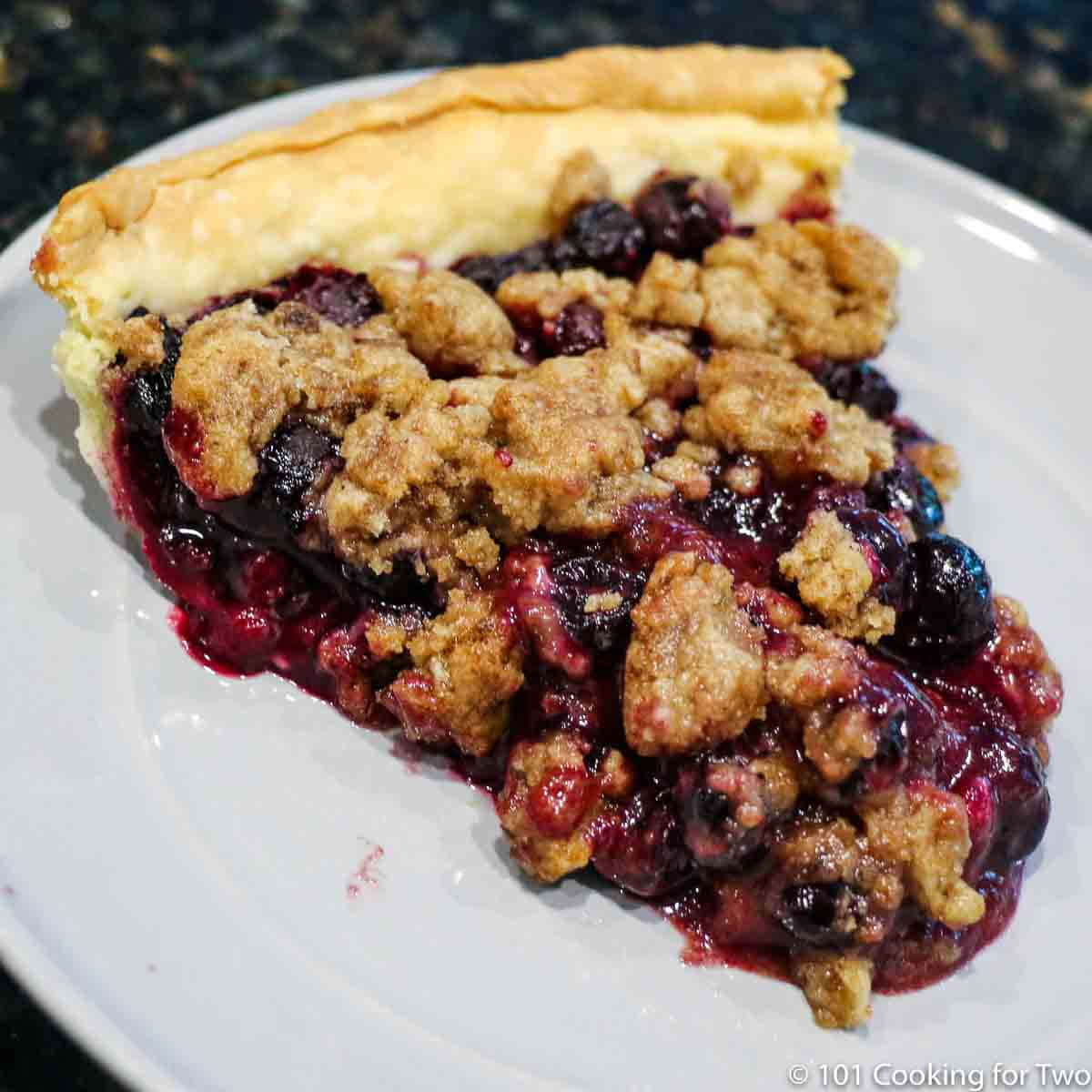 Blueberry Pie 桌布 壁紙 — 一塊藍莓金寶派的近照，金黃酥皮配上多汁莓果餡料，放在白色盤子上。