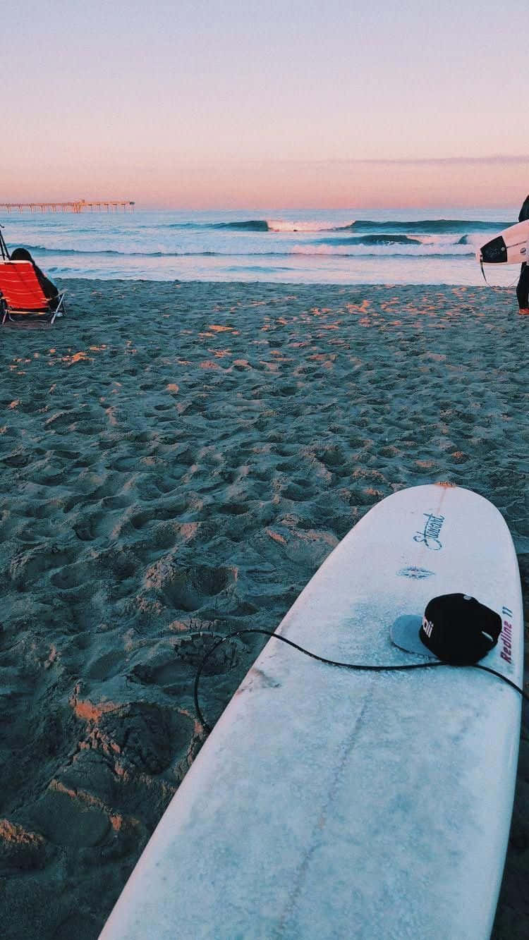 sand 桌布 壁紙 — 一塊衝浪板在黃昏時分擱在沙灘上，遠處有海浪和碼頭。