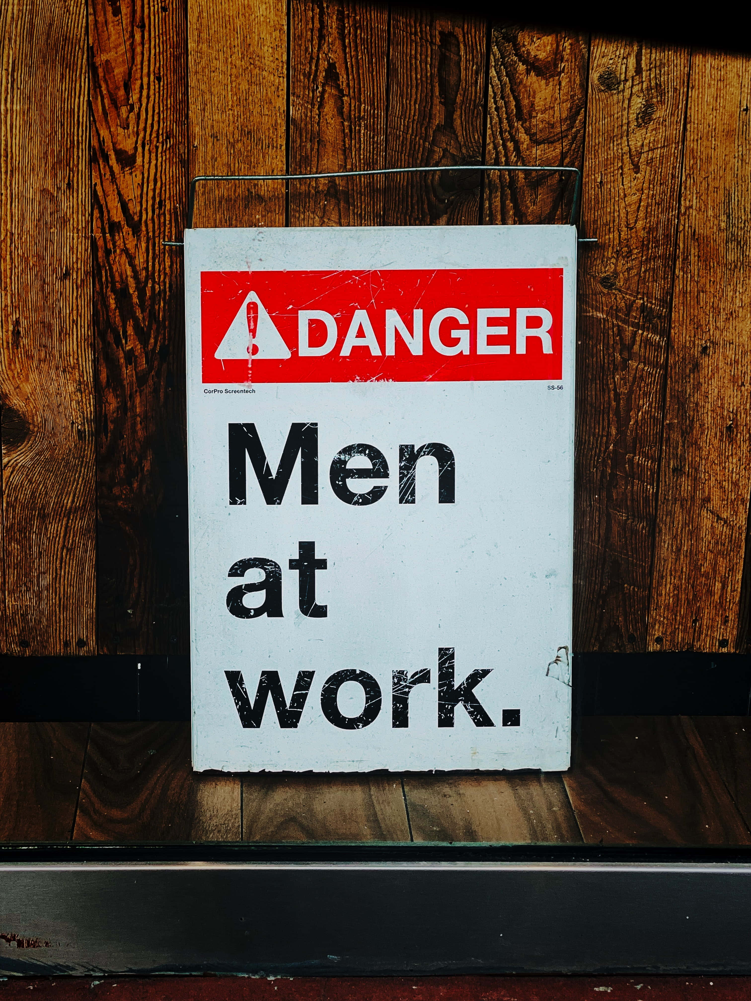 Danger 桌布 壁紙 — 一塊褪色的危險標誌，上面寫著「Men at work」，掛在帶有清晰木紋和質感的鄉村風格木牆上。