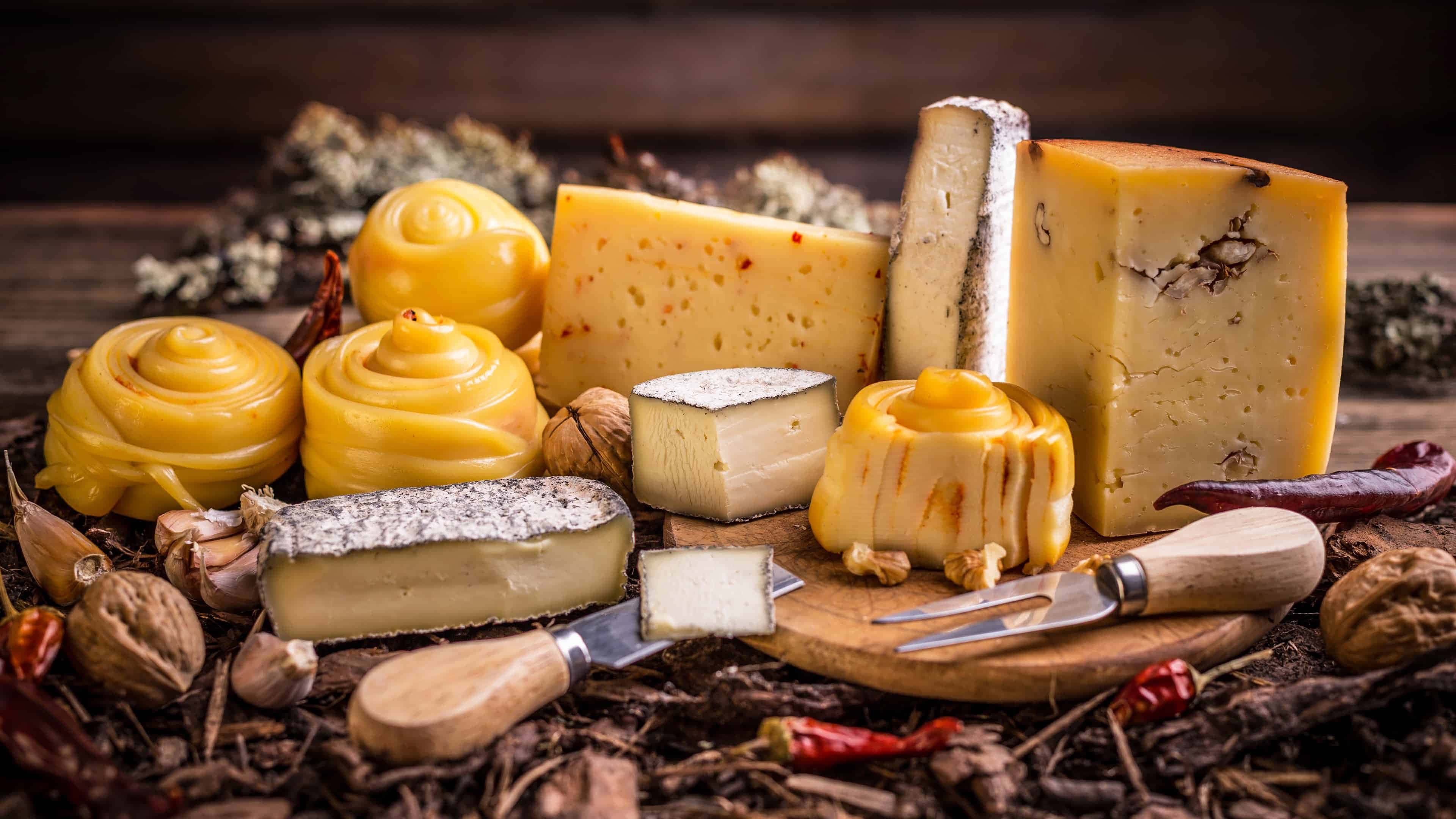 Cheese 桌布 壁紙 — 一塊質樸的木板上展示了藝術擺盤的各式起司，搭配堅果和乾辣椒。