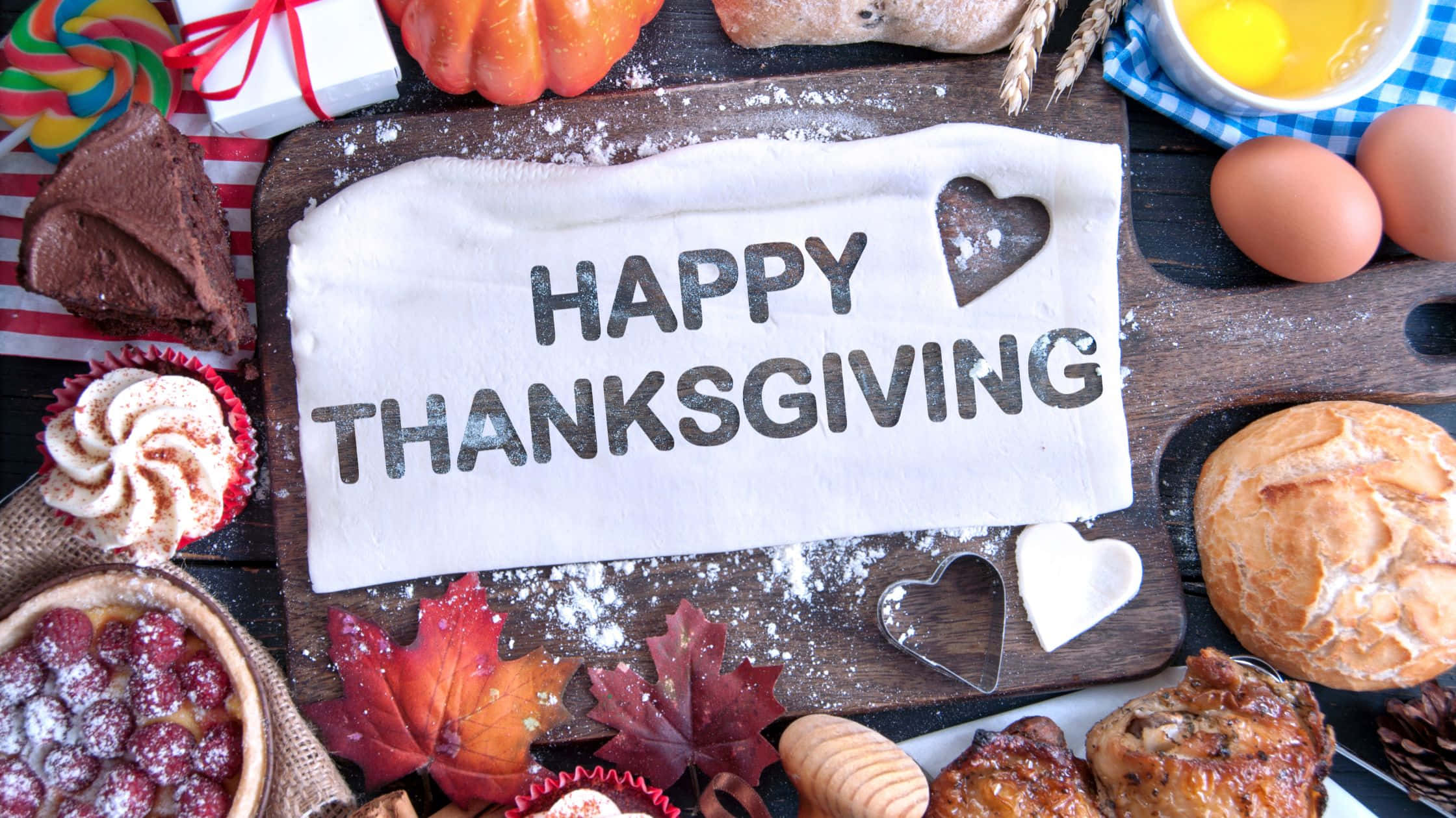 Thanksgiving Desktop 桌布 壁紙 — 一塊質樸的木板上展示著一個「HAPPY THANKSGIVING」標誌，周圍環繞著秋葉、烘焙食品和節日美食。