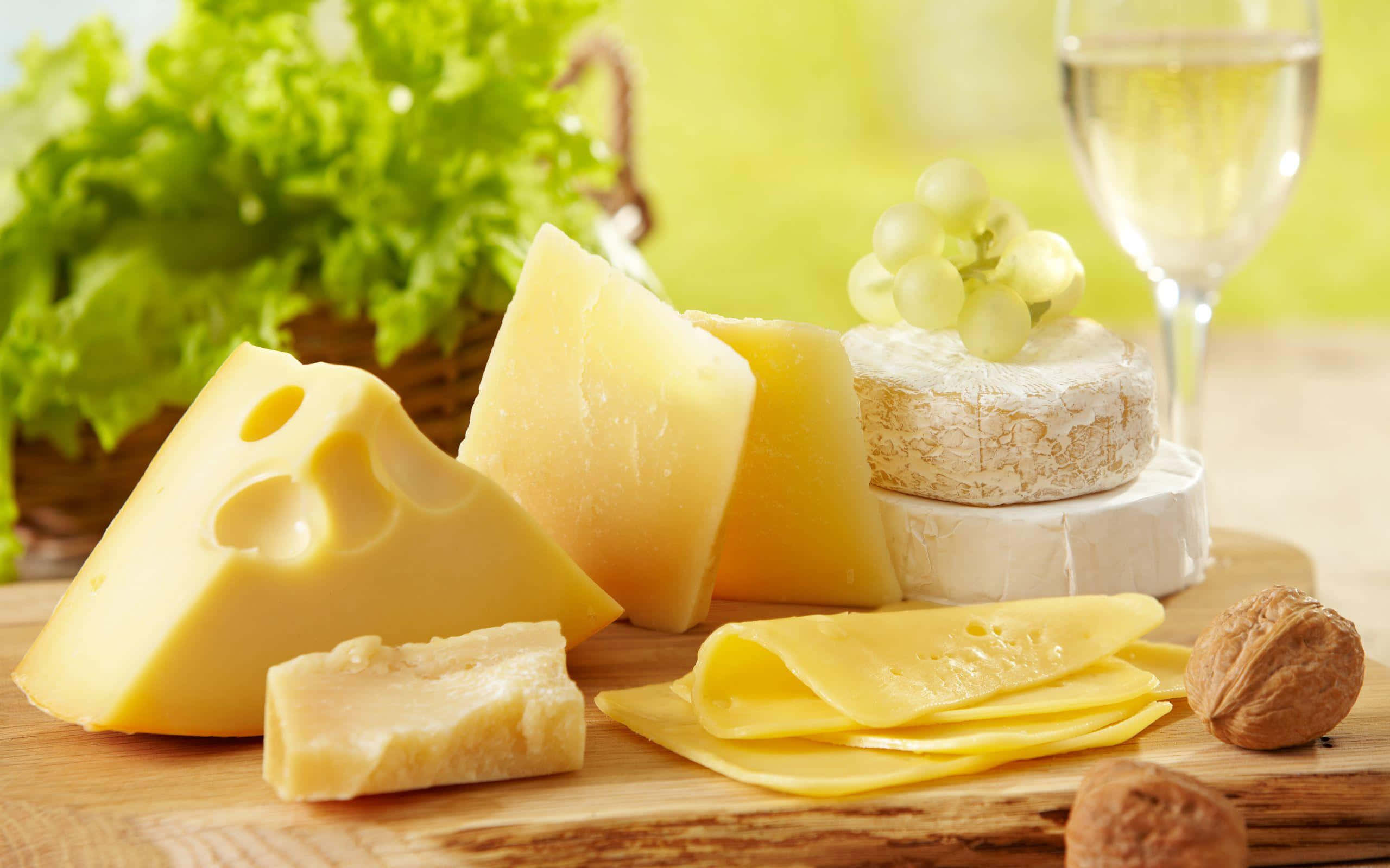 Cheese 桌布 壁紙 — 一塊質樸的木板上展示著各式起司、葡萄、堅果和一杯白酒，背景是模糊的綠色。
