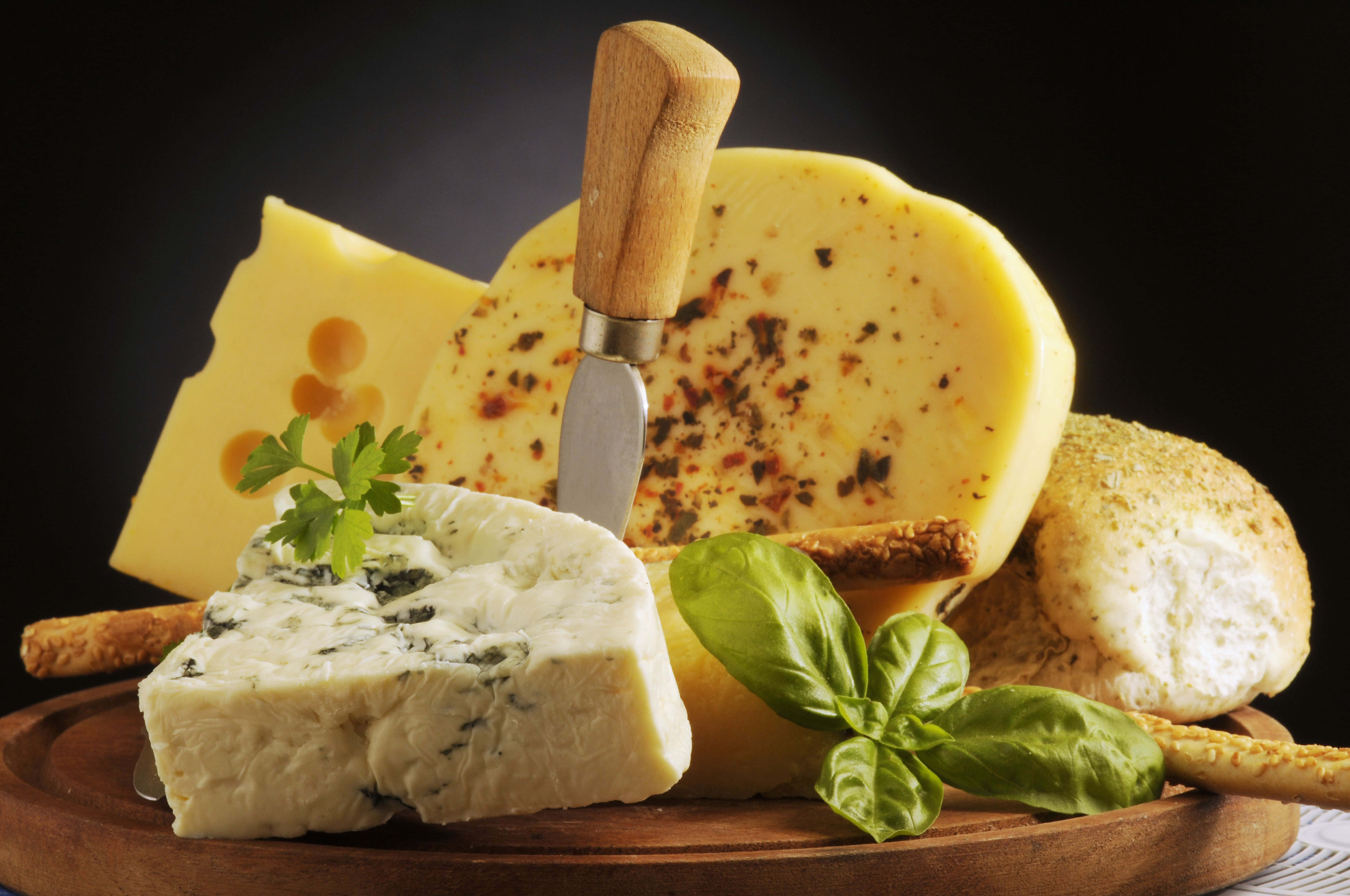 Cheese 桌布 壁紙 — 一塊質樸的木板上展示著各種起司，配以新鮮羅勒和麵包棒，背景為深色。