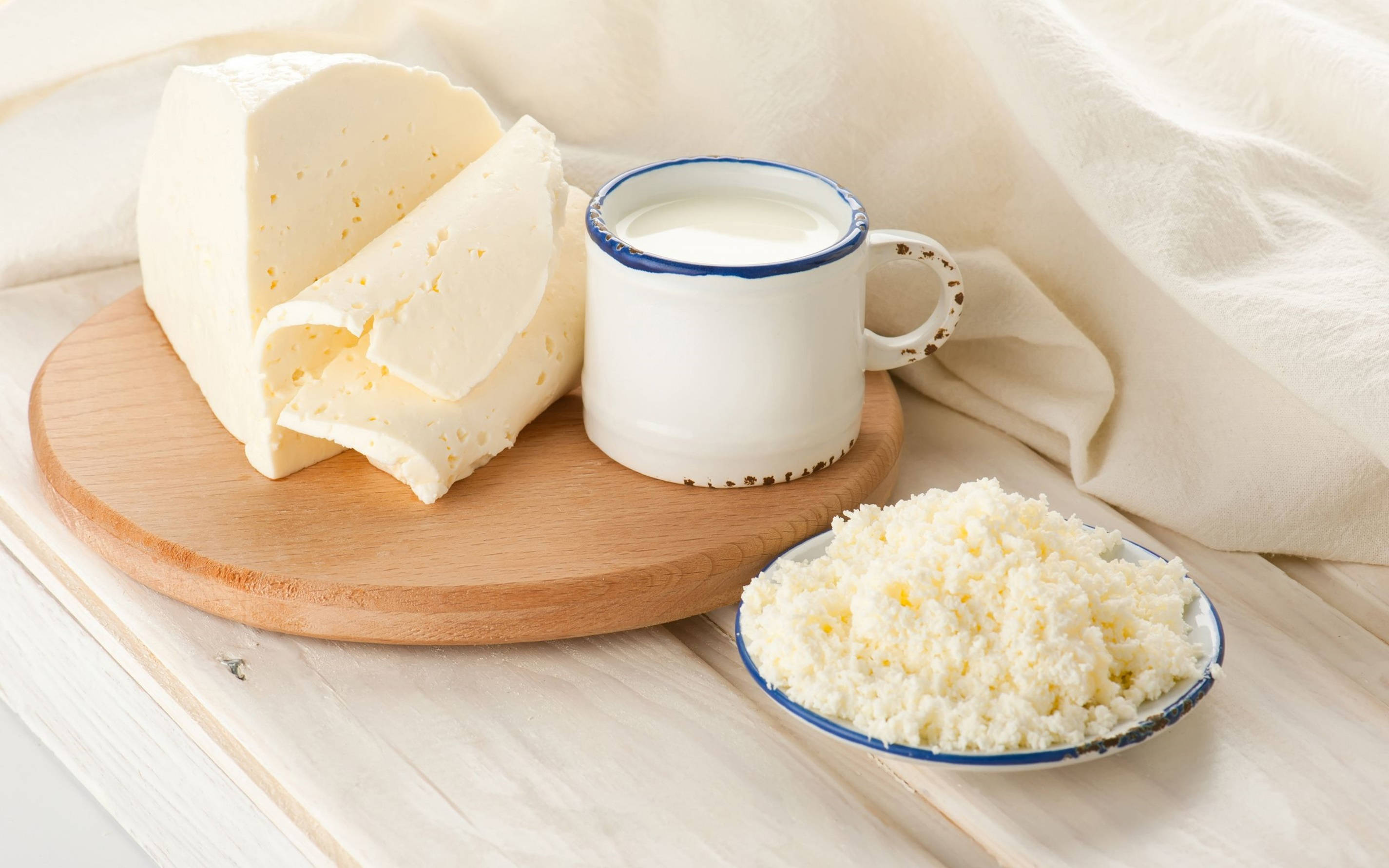 Milk 桌布 壁紙 — 一塊質樸的木板上放著奶油白起司片、一杯牛奶和一碗覆蓋著柔軟米色布料的磨碎起司。