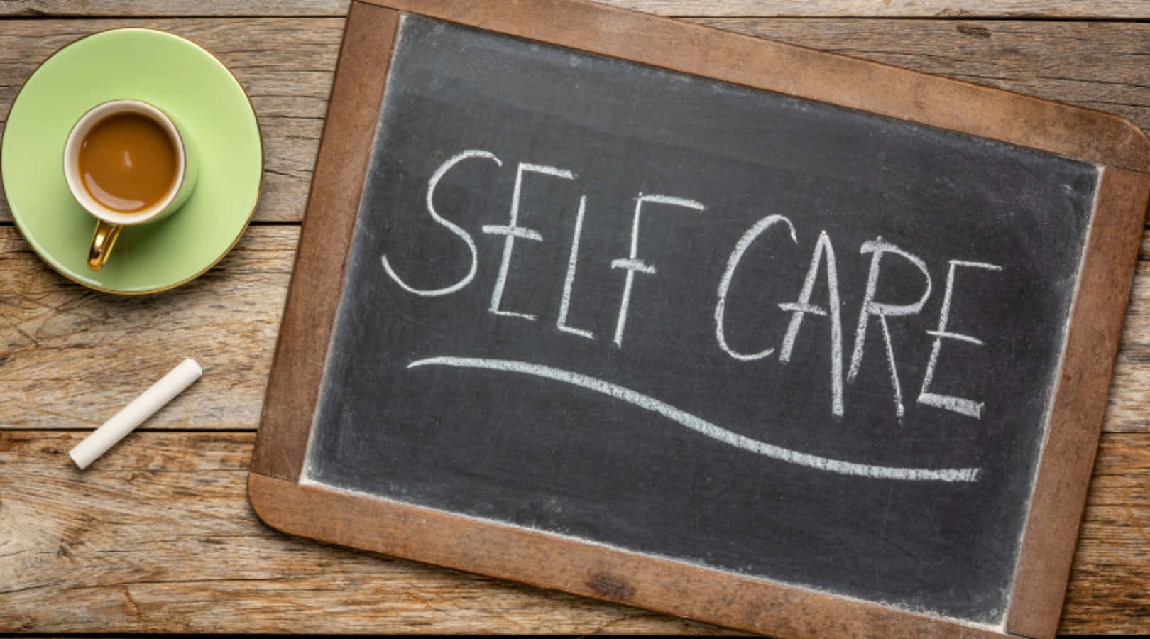 Self Care 桌布 壁紙 — 一塊質樸的黑板上用白色粉筆寫著「SELF CARE」，旁邊放著一個綠色茶碟，上面有一杯咖啡，置於經風化的木桌上。