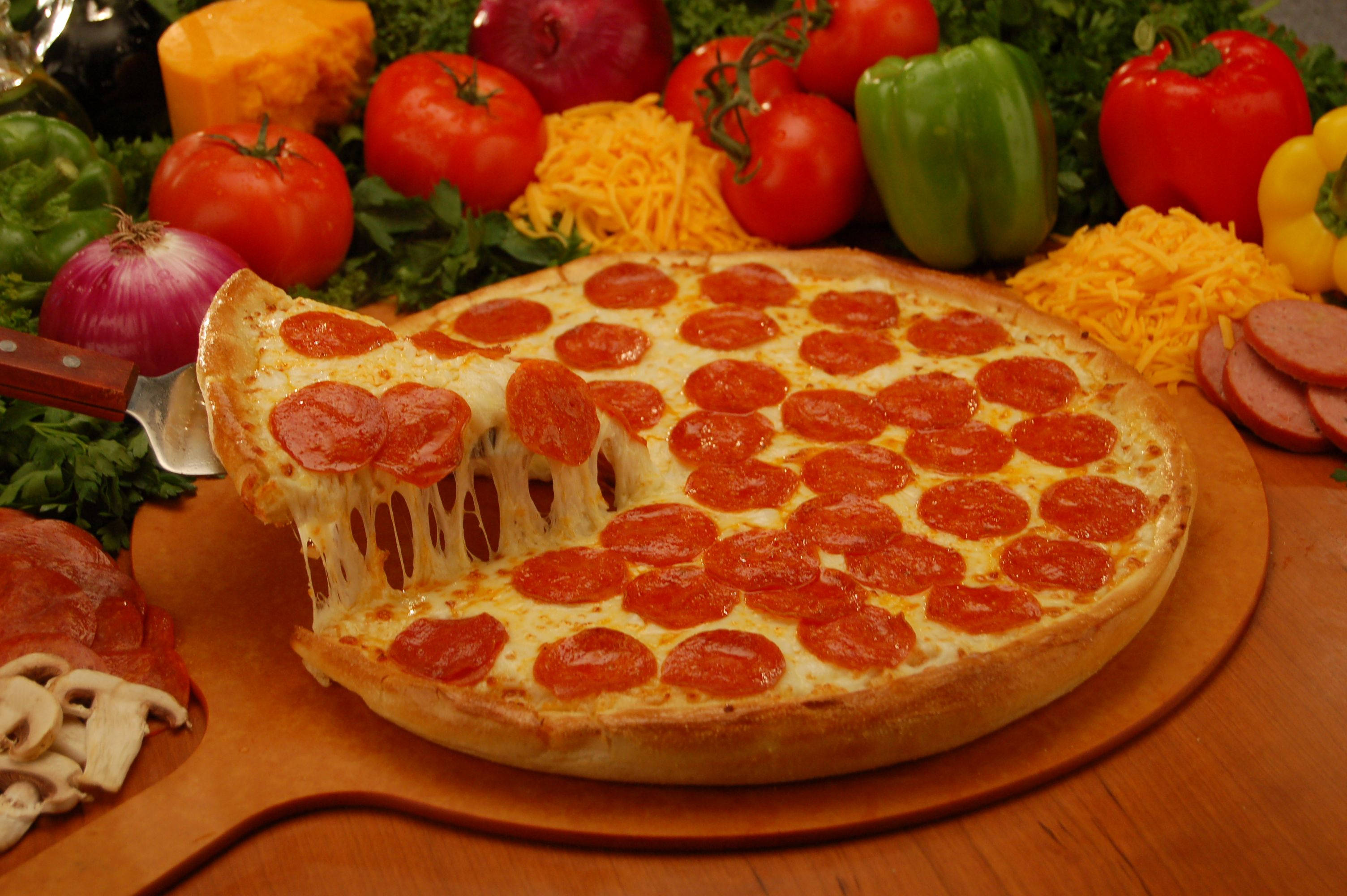Pizza 桌布 壁紙 — 一塊起司辣味香腸披薩，拿起一片露出牽絲起司，周圍是新鮮蔬菜和肉類。