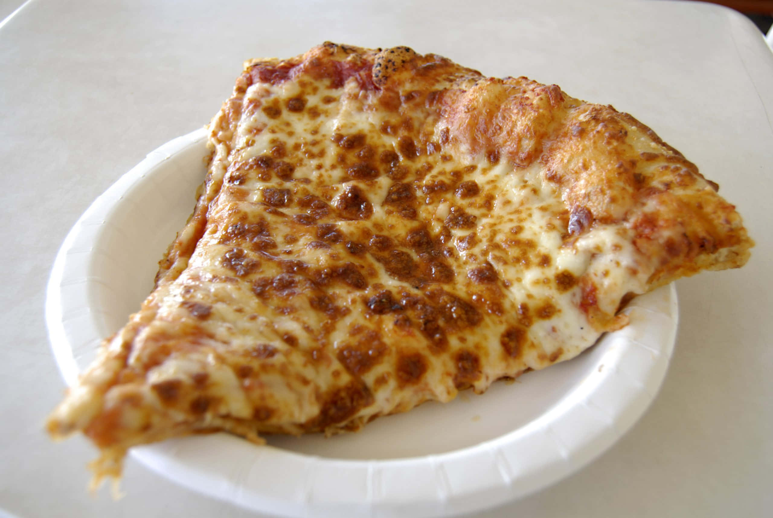 Pizza 桌布 壁紙 — 一塊起司辣肉腸披薩的特寫，放在白色紙盤上，有金黃色的脆邊。