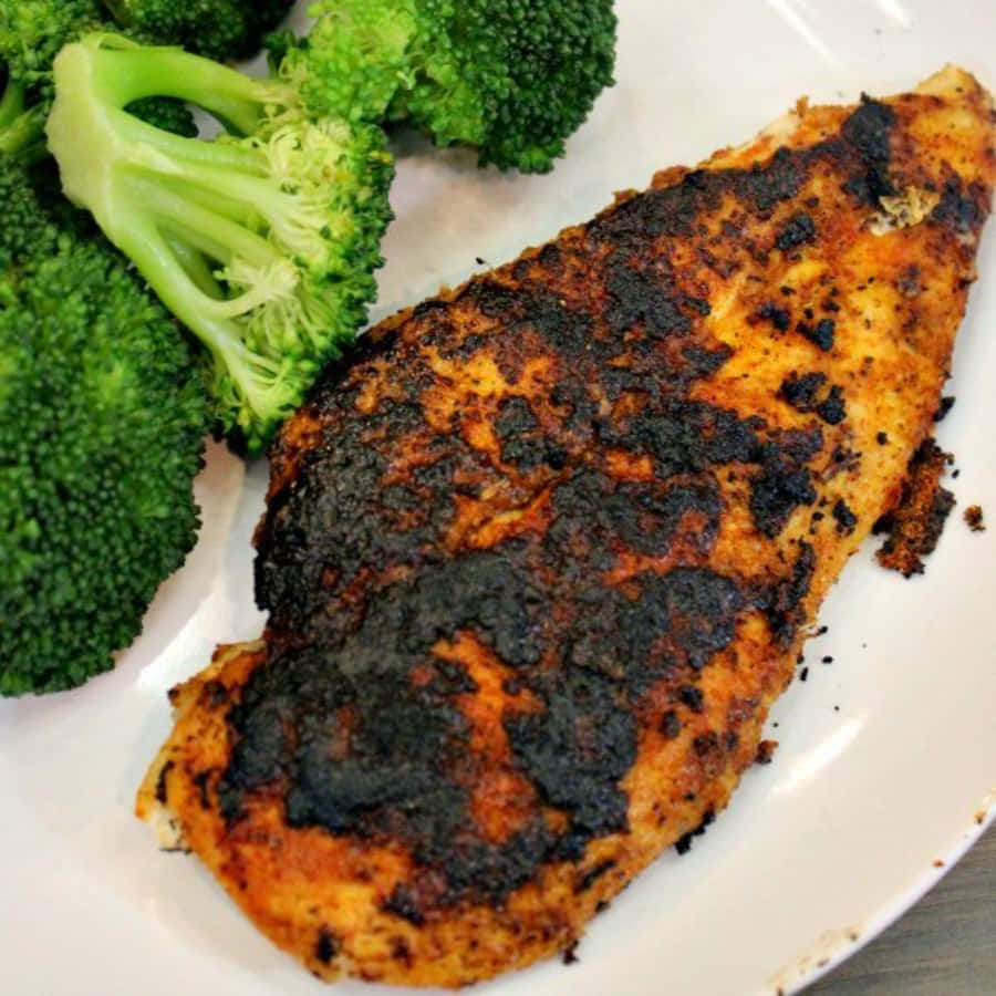 Blackened Chicken 桌布 壁紙 — 一塊邊緣焦黑的燒焦雞胸肉，放在白色盤子上，旁邊是鮮綠色的青花菜小朵。