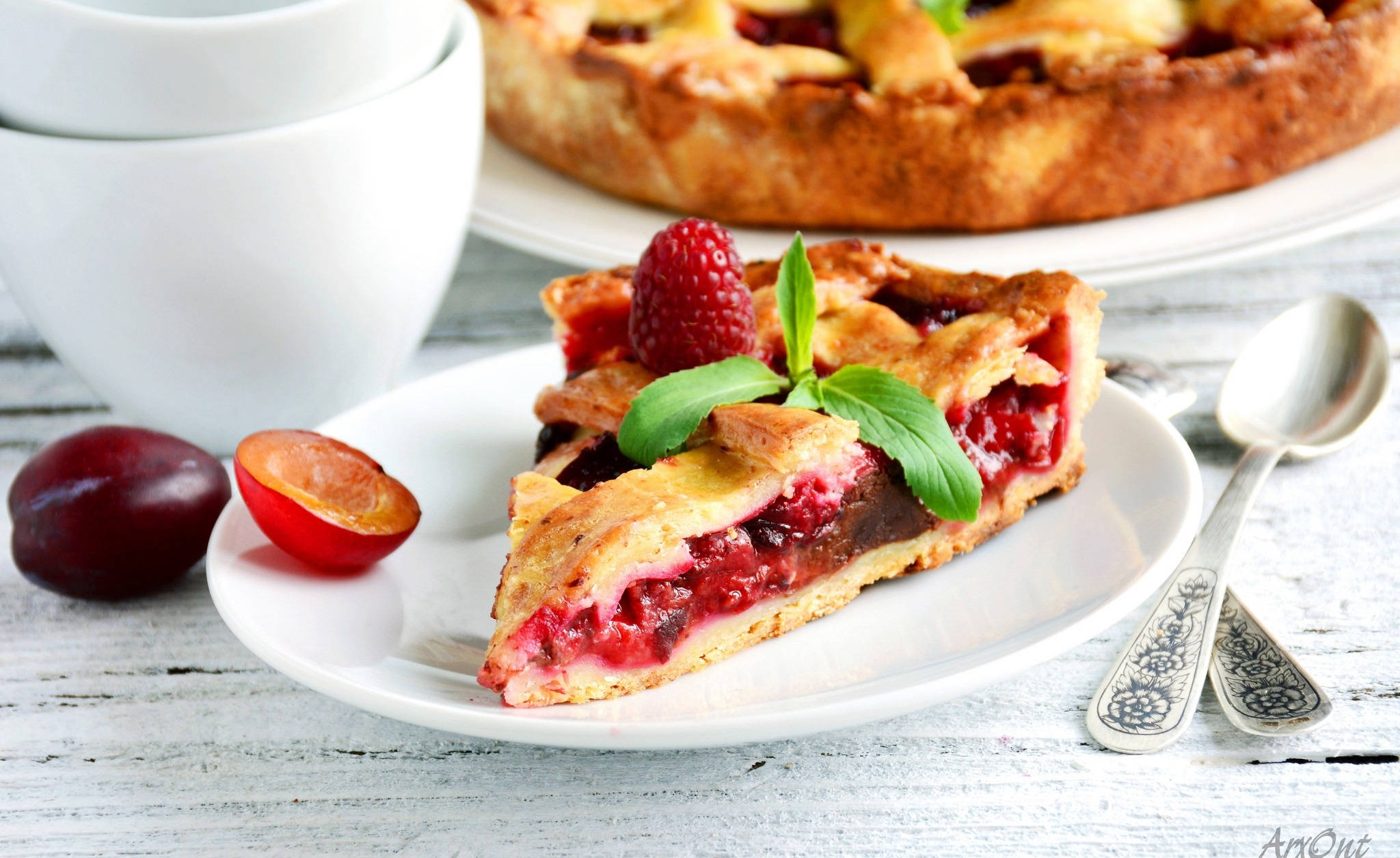 Pie 桌布 壁紙 — 一塊鄉村風味的李子塔，飾以覆盆子和薄荷，放在白色盤子上，旁邊有整個李子和裝飾湯匙，置於經風化的木桌上。