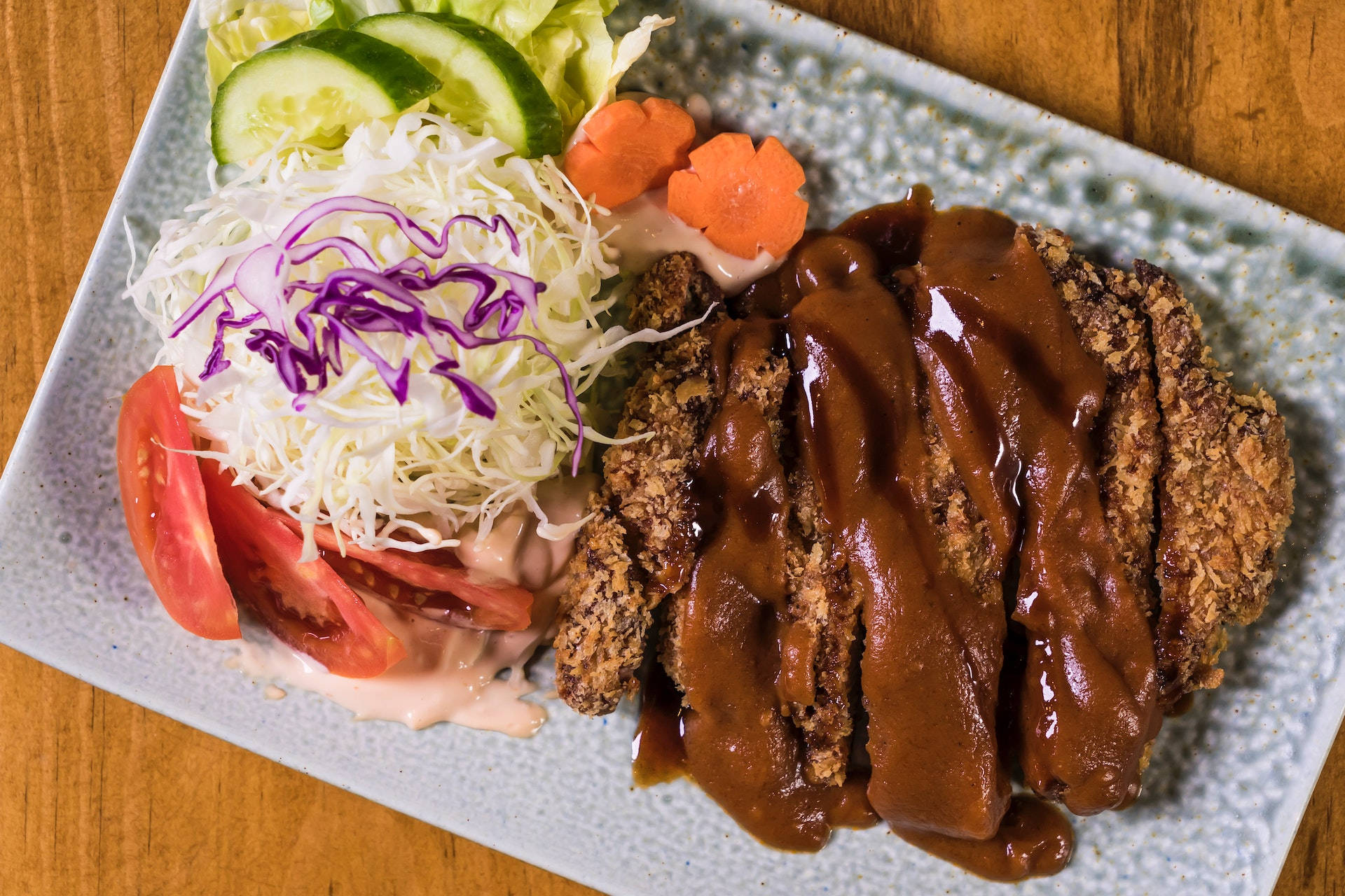 Food Photography 桌布 壁紙 — 一塊酥脆的炸肉排淋上光亮的棕色醬汁，旁邊是新鮮沙拉，放在有紋理的盤子上。