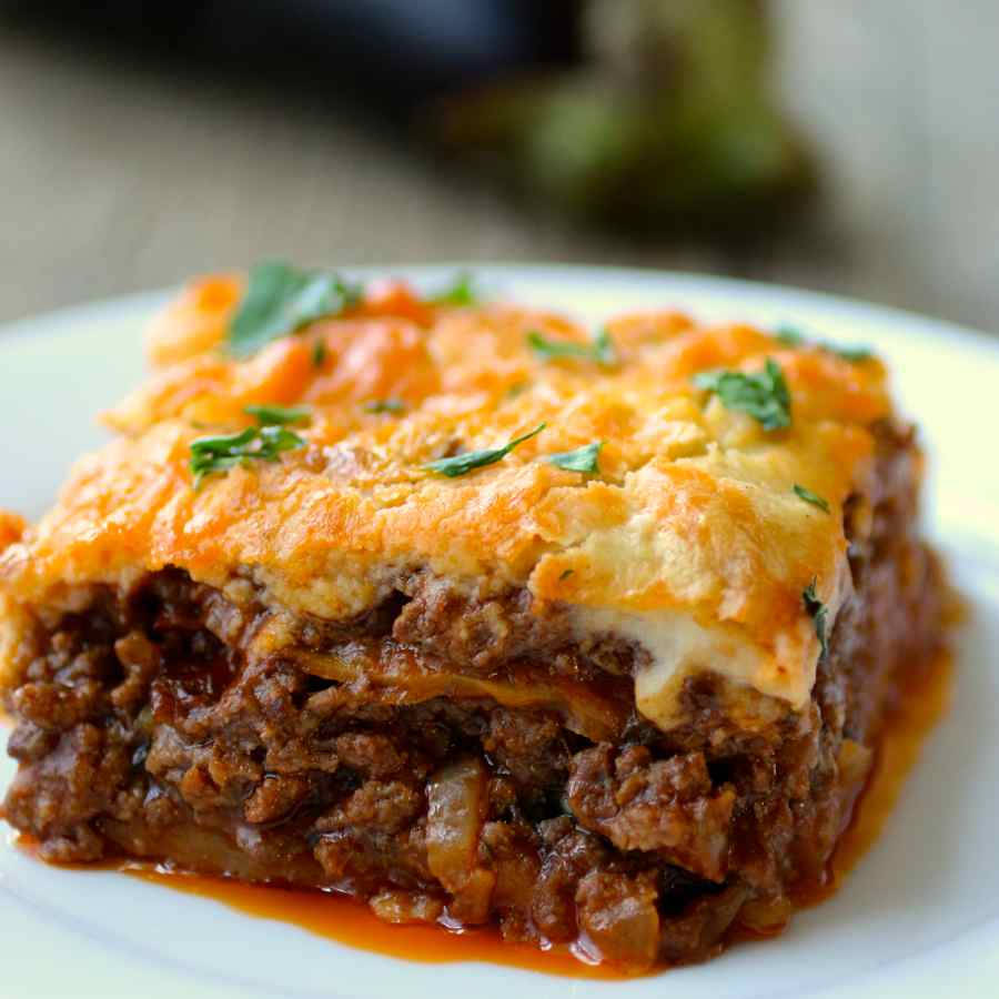 Food Photography 桌布 壁紙 — 一塊金黃色的起司肉醬千層麵，上面撒上新鮮巴西里，放在白色盤子上，周圍有濃郁的醬汁。
