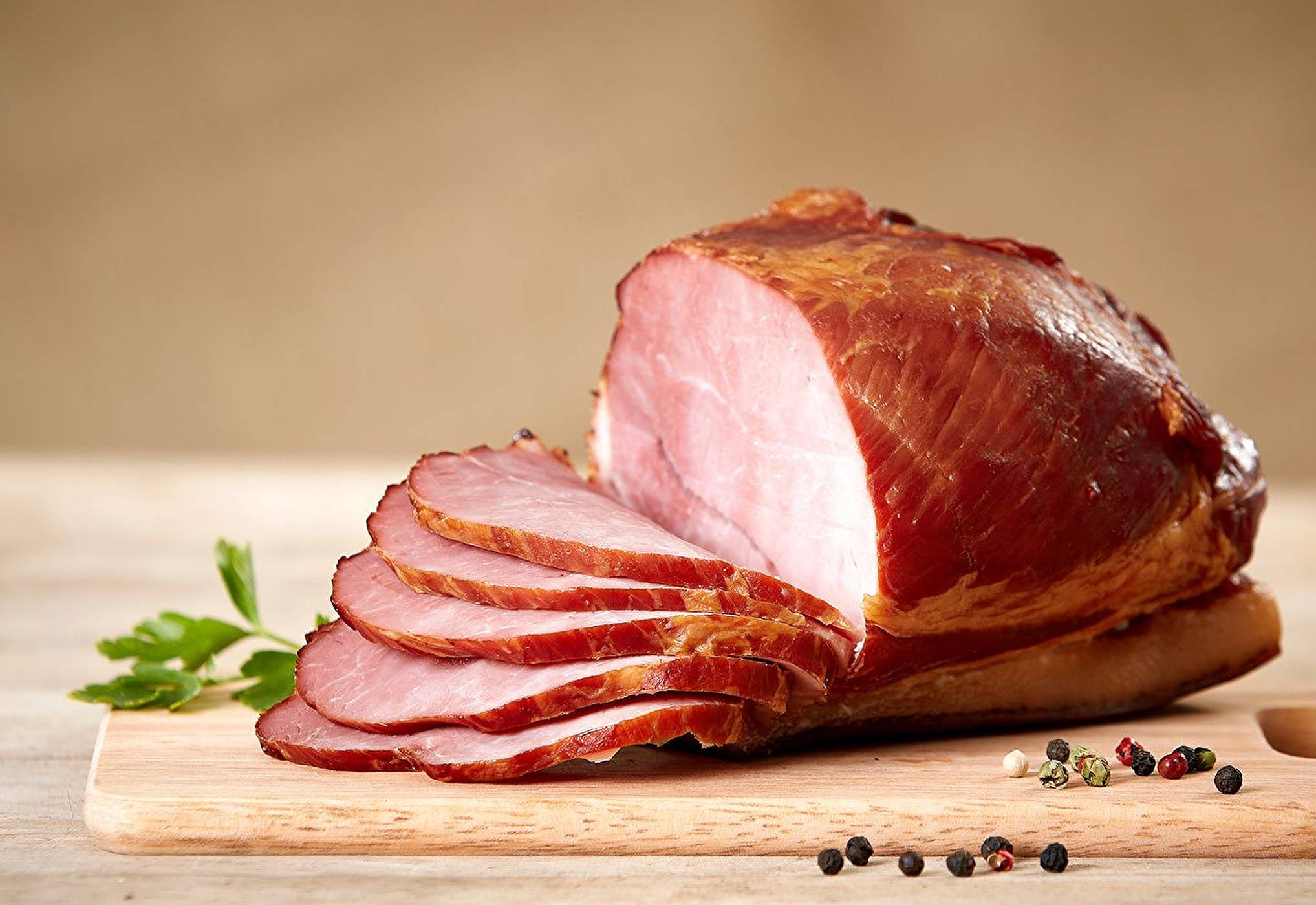 Ham 桌布 壁紙 — 一塊閃亮的烤火腿切片放在木製砧板上，旁邊是新鮮歐芹和胡椒粒。
