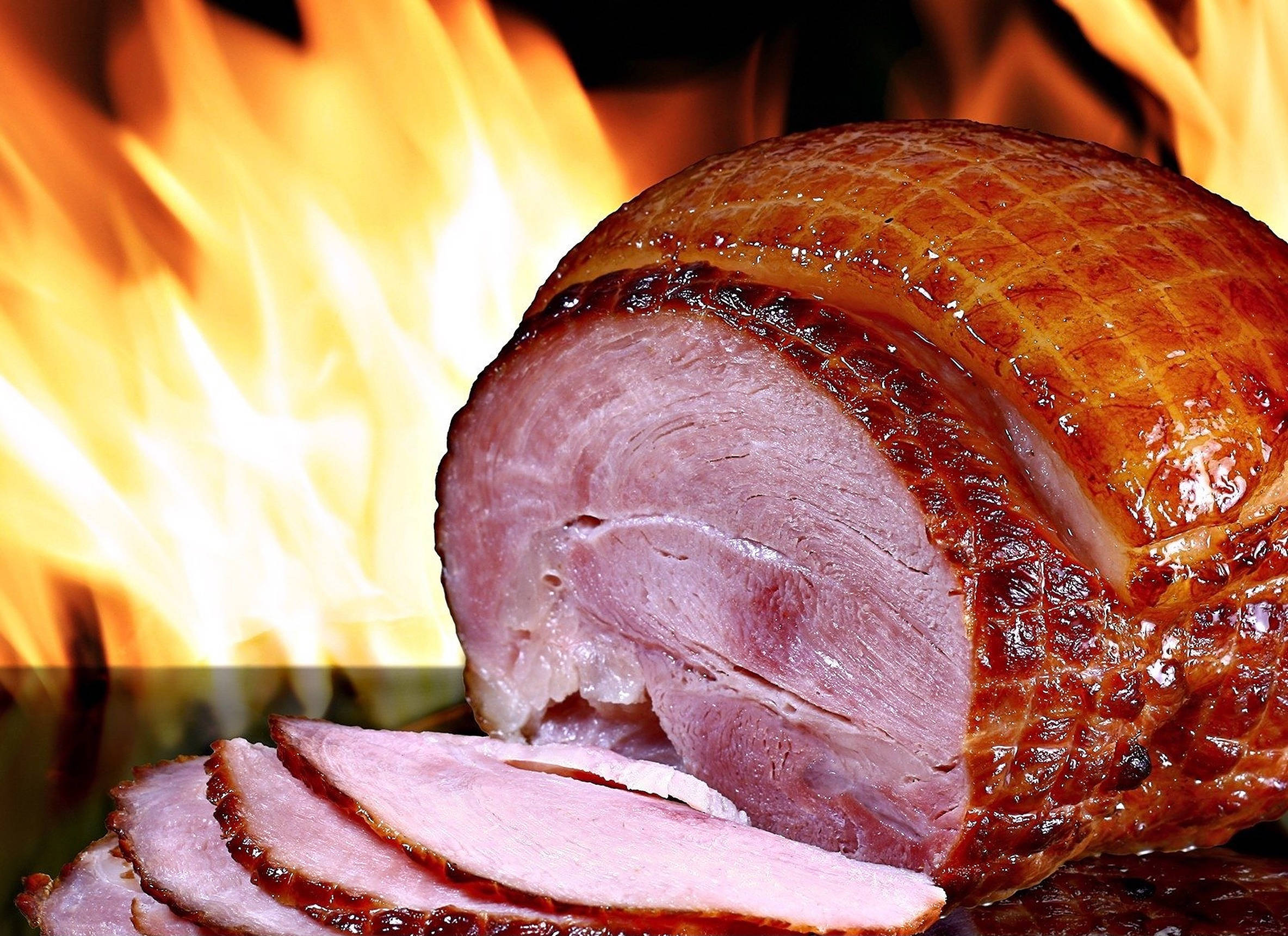 Ham 桌布 壁紙 — 一塊閃亮的烤火腿切片放在熊熊烈火前，烈火散發出溫暖的金色光芒。