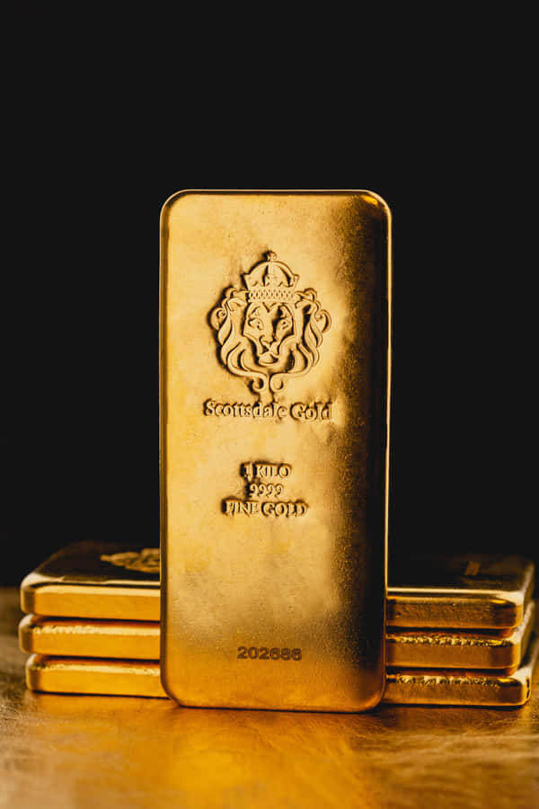 Shiny Gold 桌布 壁紙 — 一塊閃閃發光的一公斤金條，帶有獅子徽章，直立於黑色背景前，兩側堆疊著類似的金條，置於反光的金色表面上。