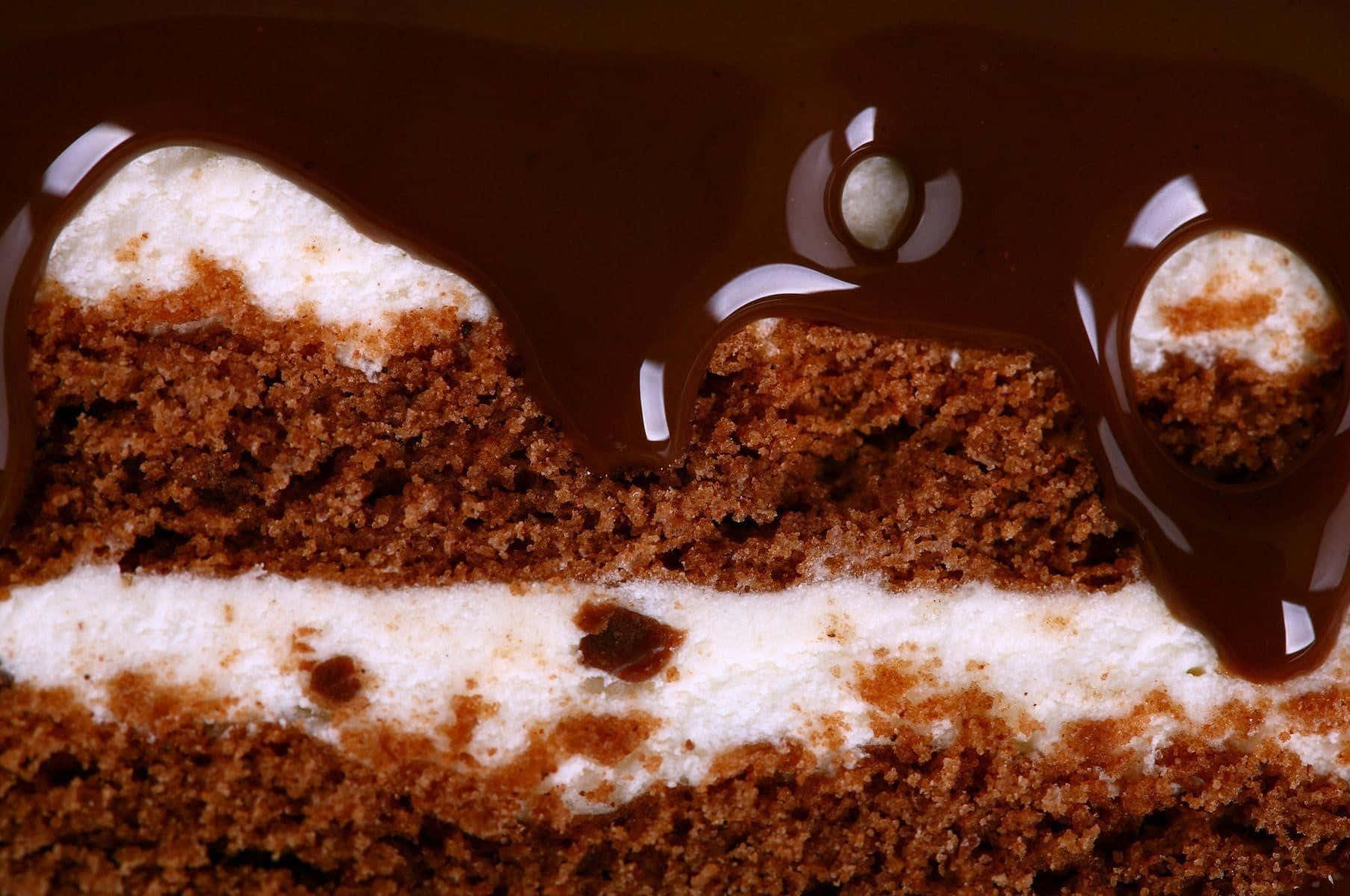 Chocolate Cake 桌布 壁紙 — 一塊頹廢的巧克力蛋糕，光澤的甘納許滴落在濕潤的蛋糕層和奶油白色糖霜上。