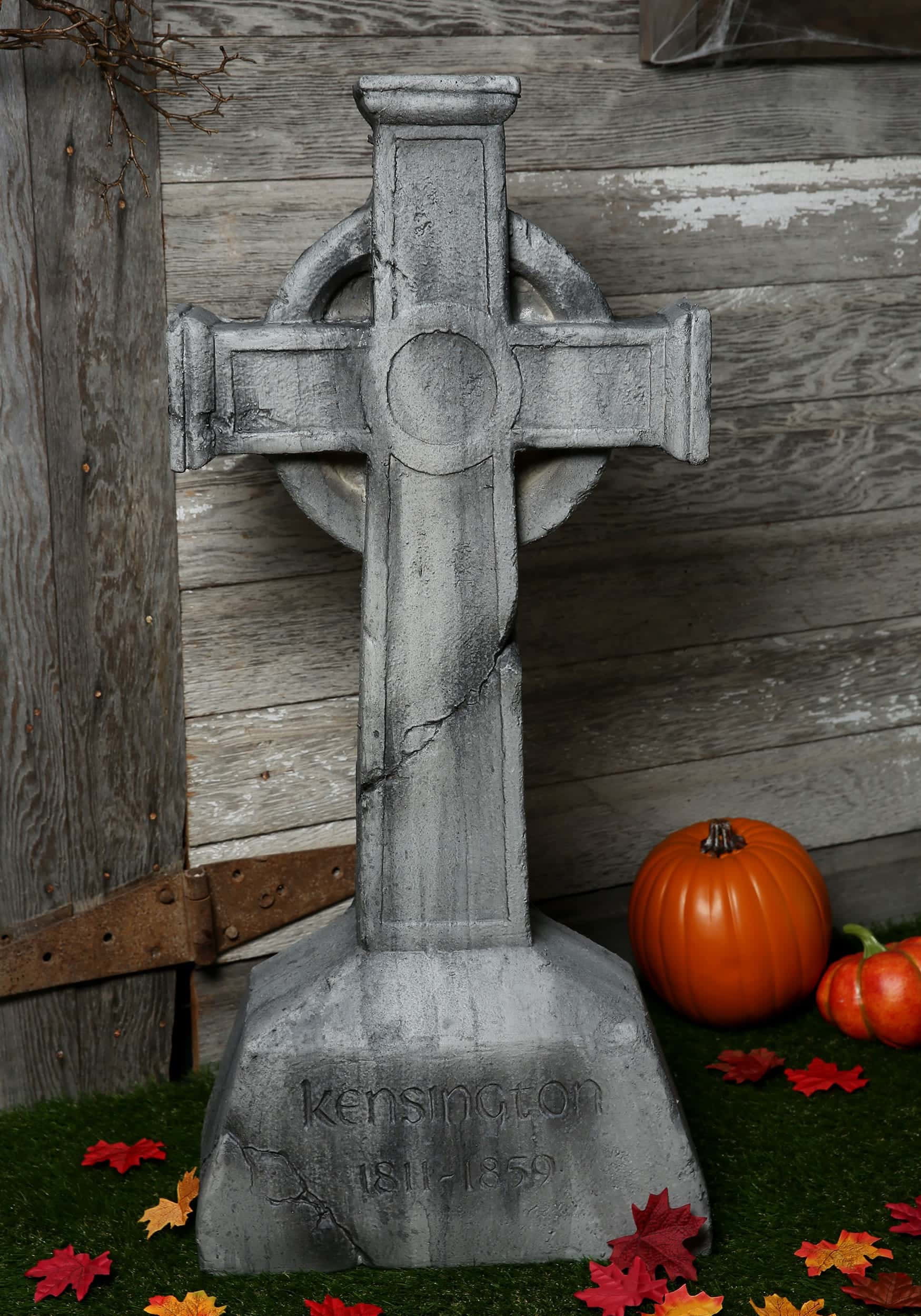 Gravestone 桌布 壁紙 — 一塊風化的凱爾特十字墓碑，刻有名字和日期，旁邊擺放著南瓜和秋葉，背景是質樸的木牆。
