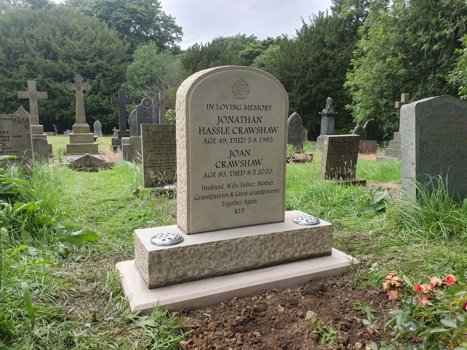 Gravestone 桌布 壁紙 — 一塊風化的灰色墓碑，在一個被樹木和其他墓碑環繞的草地墓園中，紀念喬納森·哈塞爾·克勞肖和瓊·克勞肖。
