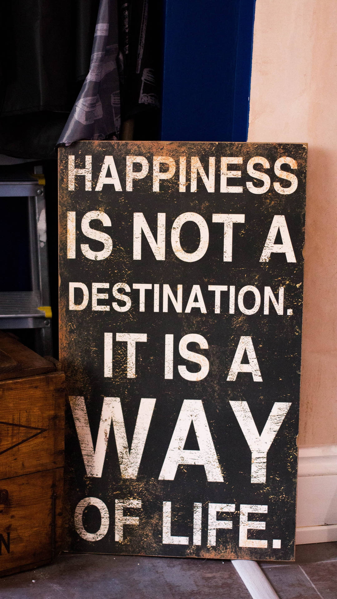Positive Quotes 桌布 壁紙 — 一塊風化的黑色木牌，上面有粗體白色文字寫著「幸福不是目的地。它是一種生活方式。」靠在室內鄉村風格的牆上。