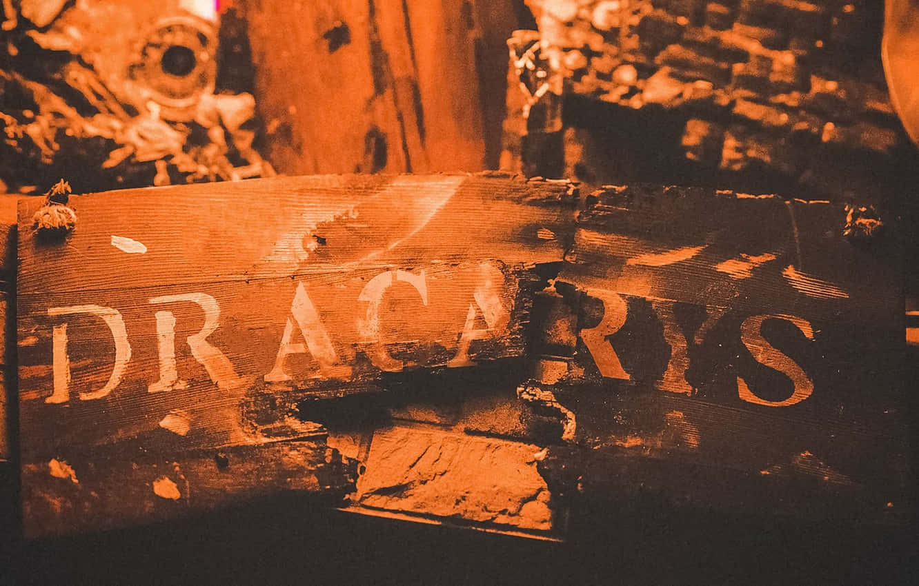 dracarys 桌布 壁紙 — 一塊飽經風霜的木牌，上面剝落的橙色油漆拼出「DRACARIS」，背景是模糊的鄉村風格。