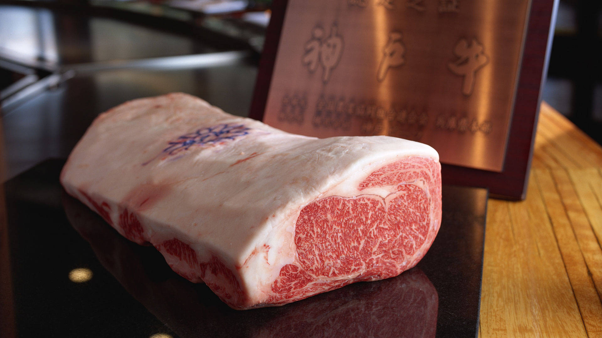 meat 桌布 壁紙 — 一塊高品質的神戶牛肉放在深色表面上，旁邊有一塊帶有日文字元的木牌。