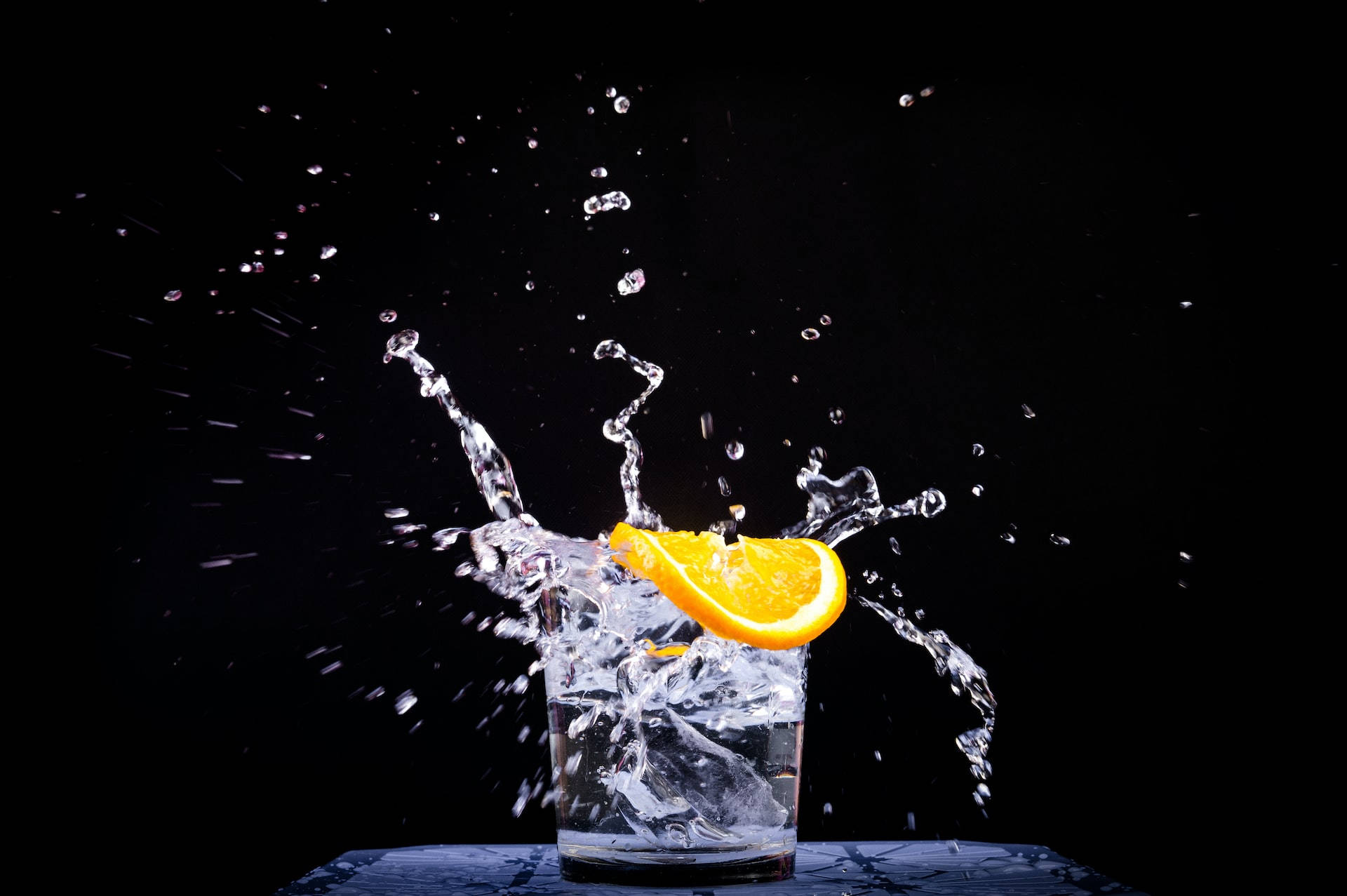Water 桌布 壁紙 — 一塊鮮豔的橙片掉進一杯水中，在純黑背景上形成戲劇性的水花。