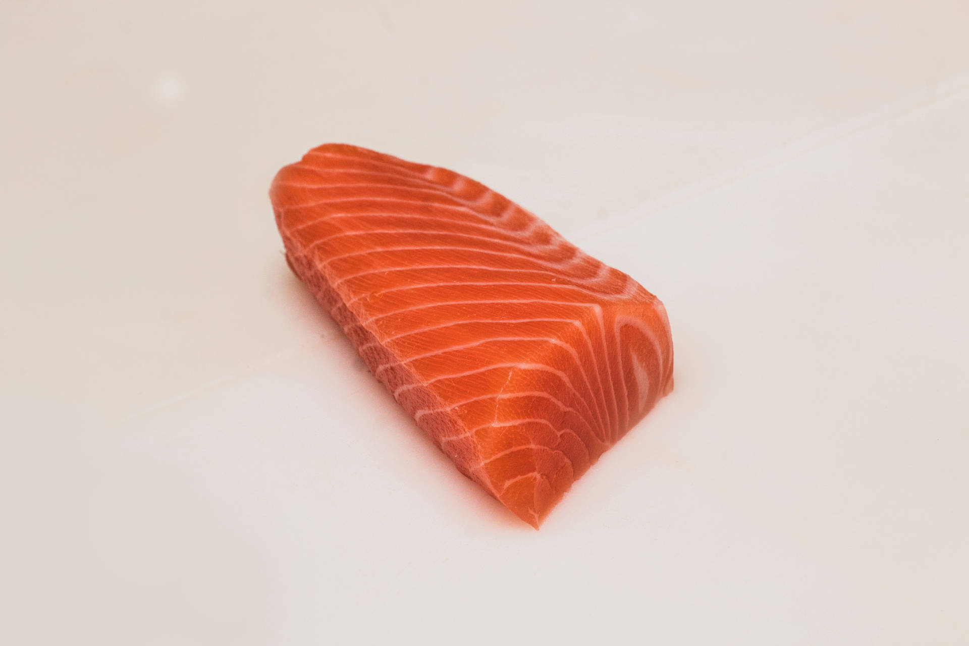 Salmon 桌布 壁紙 — 一塊鮮豔的橙色鮭魚片，帶有明顯的白色大理石紋，放在潔白的表面上。