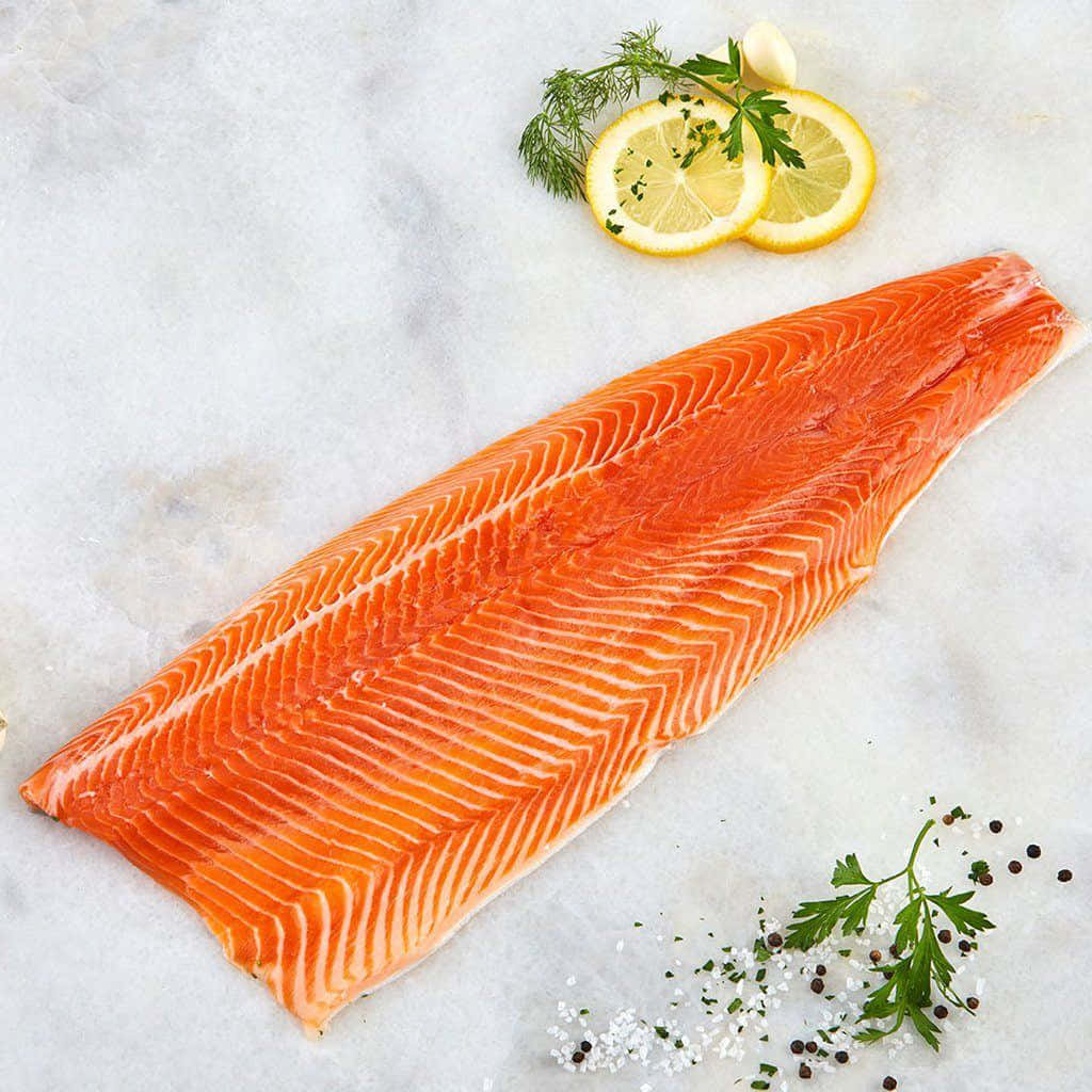 Salmon 桌布 壁紙 — 一塊鮮豔的橙色鮭魚片放在白色大理石表面上，旁邊有檸檬片、新鮮香草和鹽胡椒。