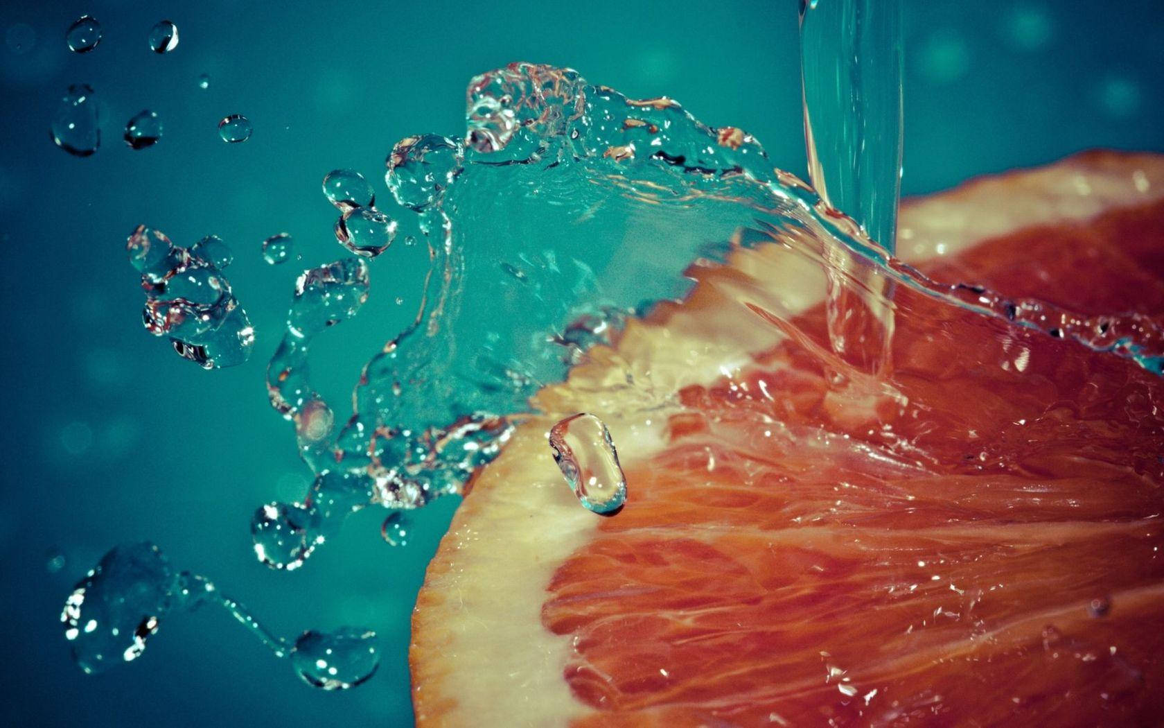 Water Splash 桌布 壁紙 — 一塊鮮豔的葡萄柚片，被清澈的水潑濺，背景為青綠色。