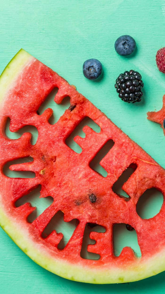 預科生美學 桌布 壁紙 — 一塊鮮豔的西瓜片刻有「HELLO SUMMER」，旁邊放有藍莓、黑莓和覆盆子，置於青綠色的木質表面上。