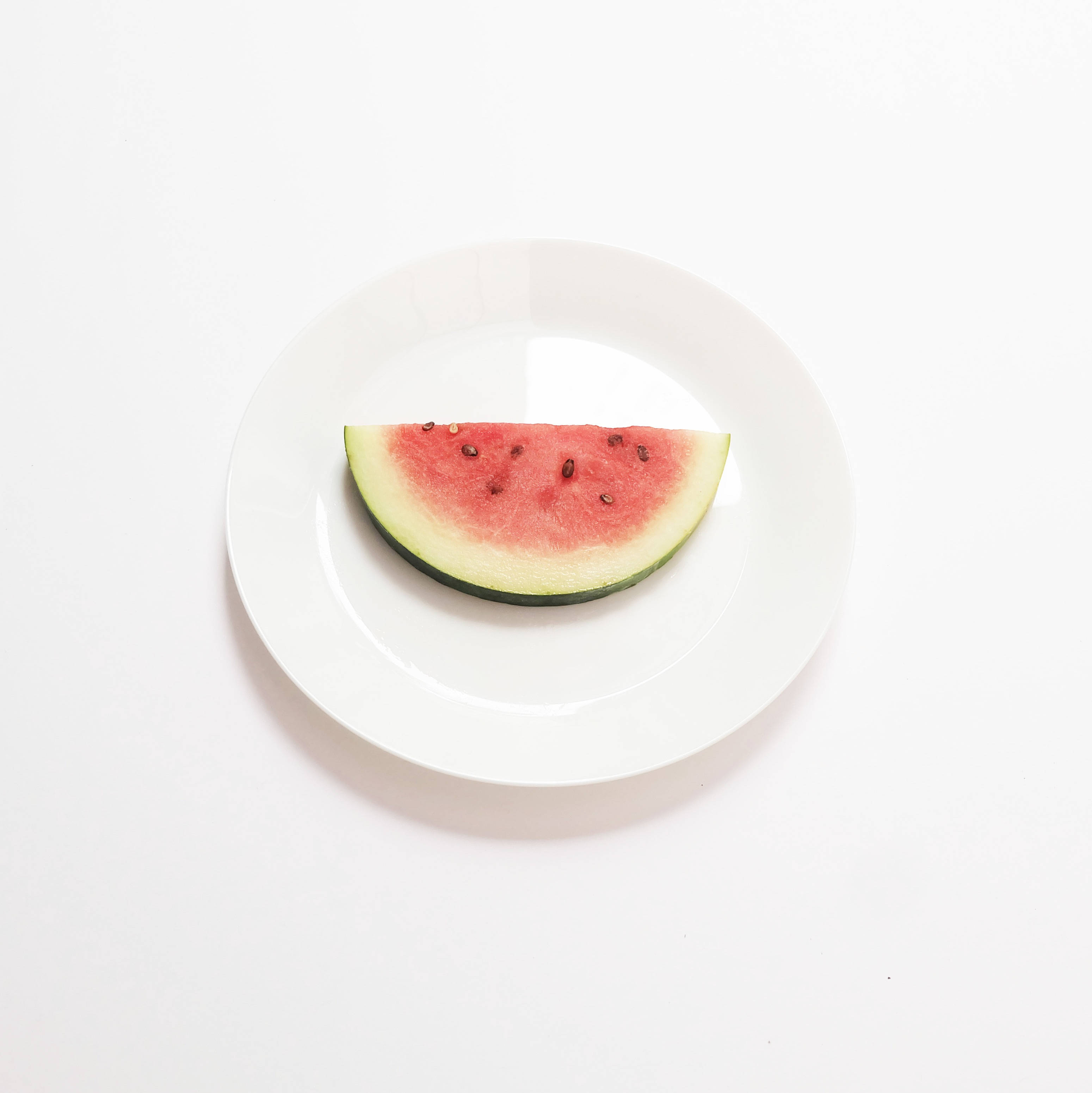 Watermelon 桌布 壁紙 — 一塊鮮豔的西瓜片放在潔淨的白色盤子上，背景是乾淨的白色。
