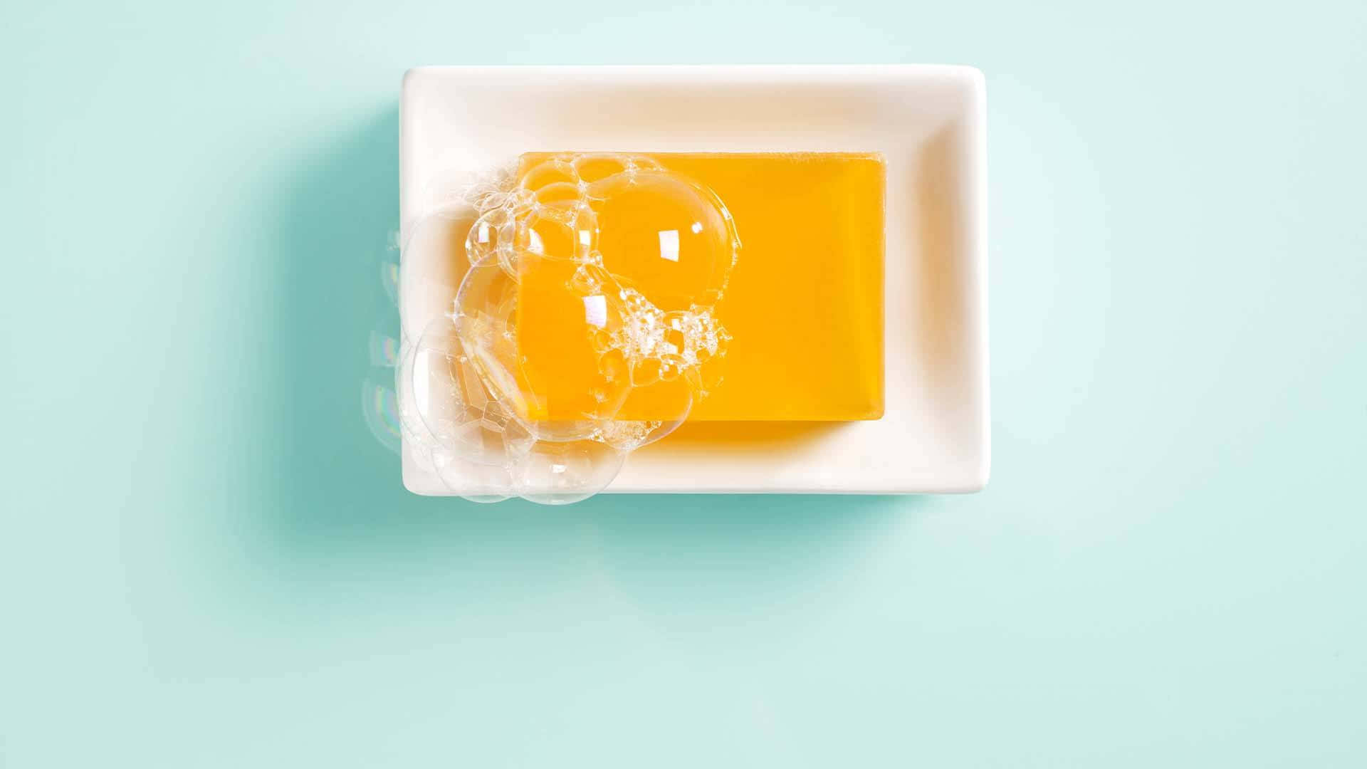 淺藍色 桌布 壁紙 — 一塊鮮黃色肥皂帶有清澈氣泡，放在白色碟中，背景是柔和的薄荷綠色。