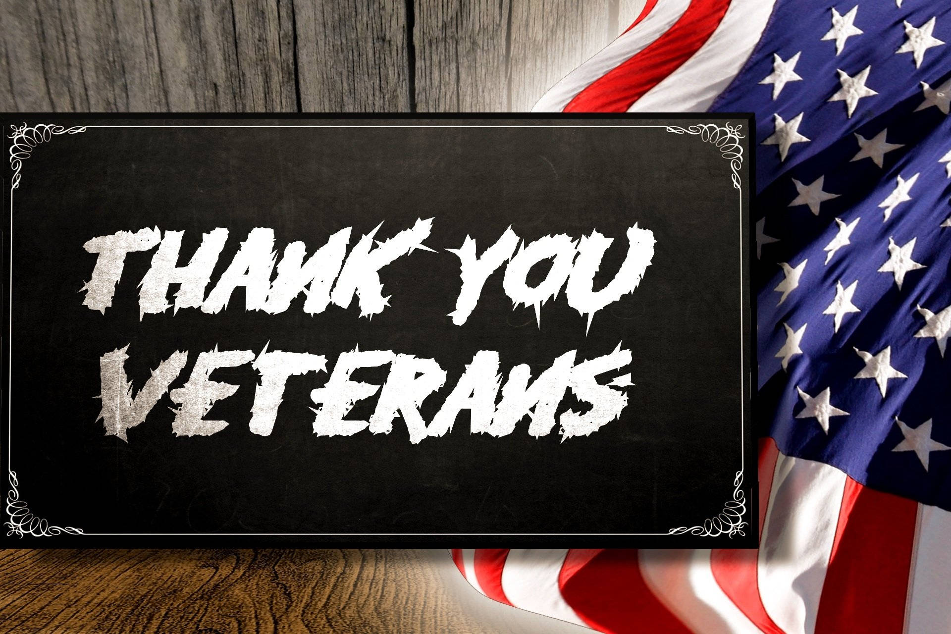Veterans 桌布 壁紙 — 一塊黑板，上面有粗體白色「THANK YOU VETERANS」文字，放在木質表面上，旁邊是垂掛的美國國旗。
