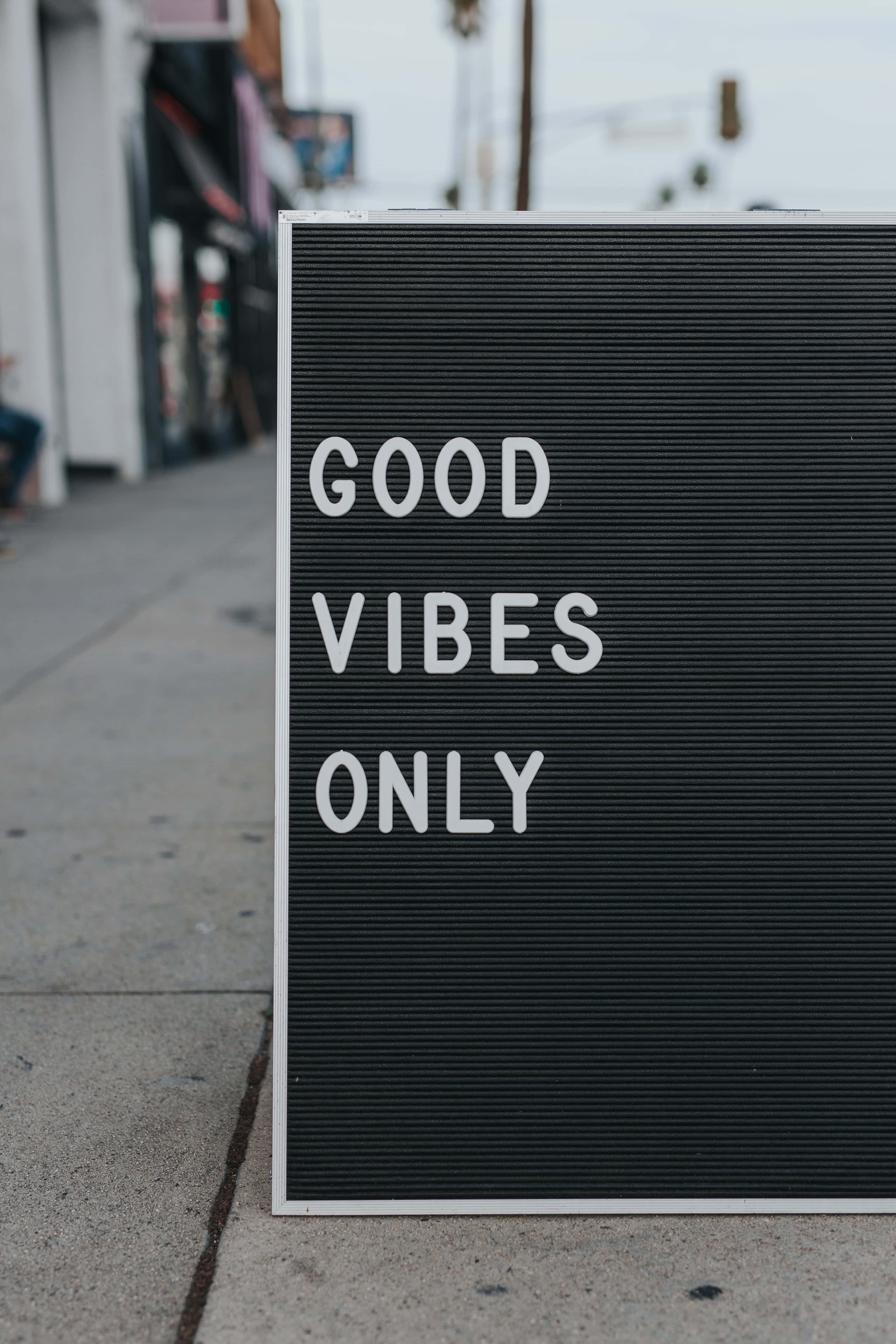 Outside 桌布 壁紙 — 一塊黑色字母板放在人行道上，大膽地以白色字母顯示「GOOD VIBES ONLY」，背景是模糊的城市景觀。
