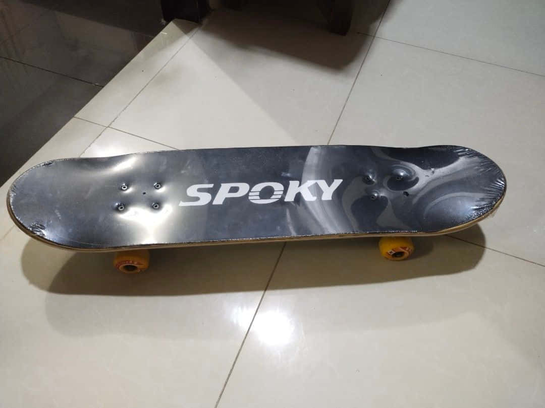 桌布 壁紙 — 一塊黑色滑板，帶有白色「SPOKY」品牌標誌和黃色輪子，在室內燈光下放置於瓷磚地板上。