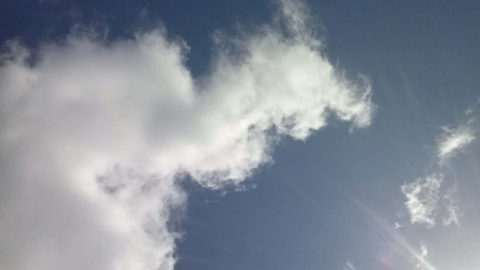 CLOUD-16 壁紙 — 一大片蓬鬆的白雲在深藍色的天空中飄移，微弱的陽光穿透雲層。