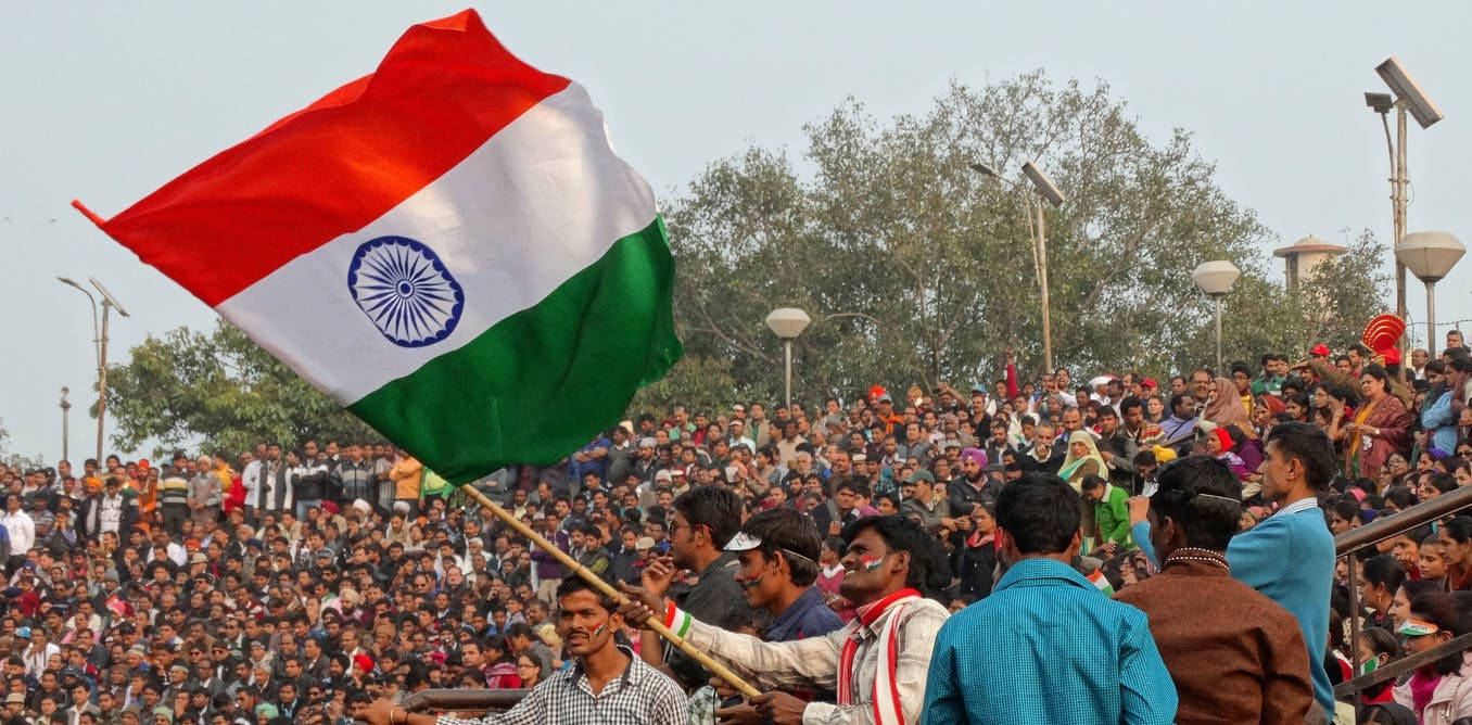 Indian 桌布 壁紙 — 一大群人聚集在戶外，一人揮舞著一面帶有紅、白、綠條紋和藍色阿育王法輪的大型印度國旗。