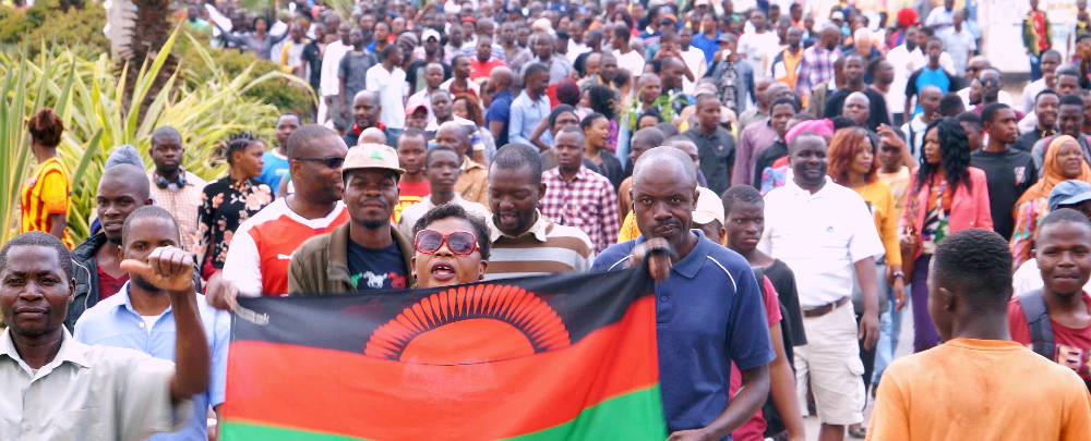 Malawi 桌布 壁紙 — 一大群人聚集在戶外，手持馬拉威國旗，舉起拳頭象徵團結和民族自豪。