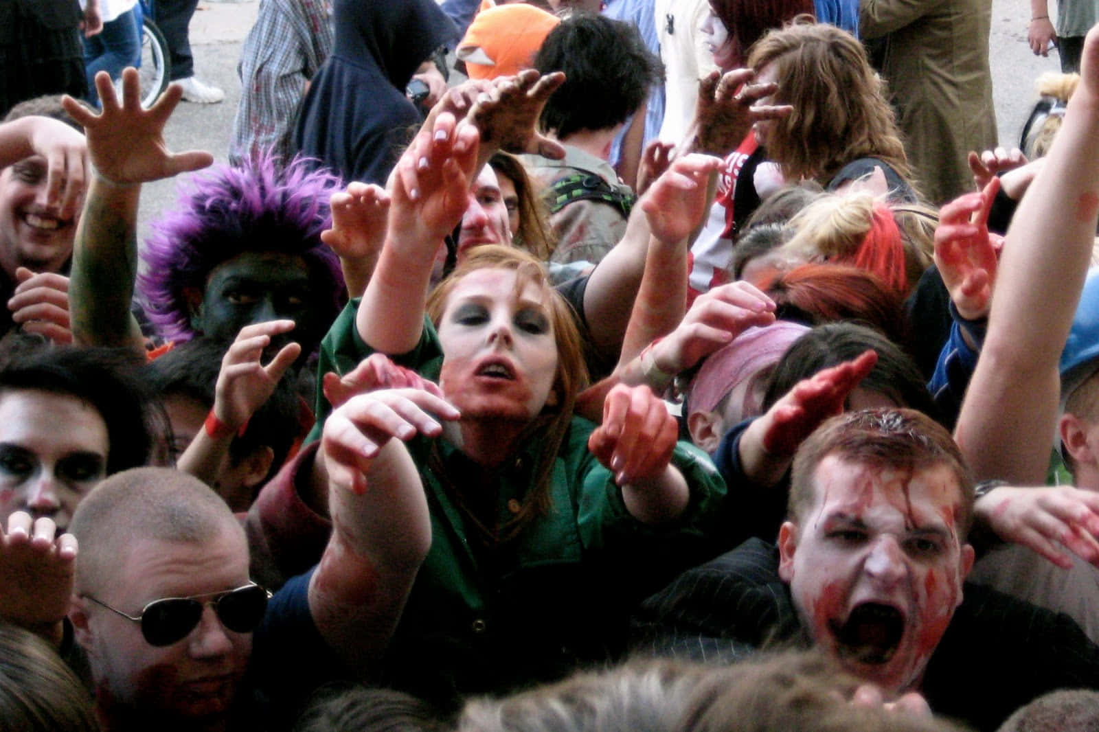 Zombie 桌布 壁紙 — 一大群化著殭屍妝容和穿著殭屍服裝的人，在熱鬧的萬聖節街頭活動中向前伸出雙手。
