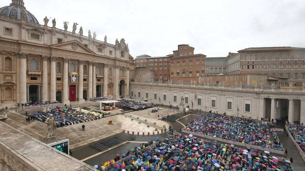 Rome 桌布 壁紙 — 一大群手持彩色雨傘的人群聚集在聖彼得廣場，天空陰沉，一位人物正在大教堂的台階上發言。