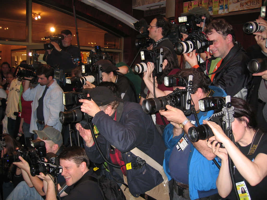 Paparazzi 桌布 壁紙 — 一大群拿著大型相機的攝影師在昏暗的室內空間中向前擠壓，捕捉一個瞬間。