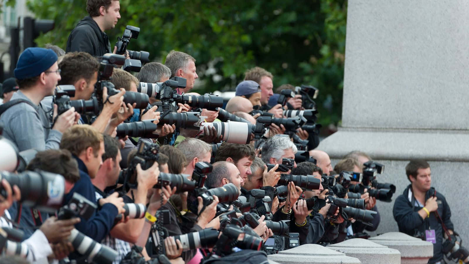 Paparazzi 桌布 壁紙 — 一大群攝影師帶著大型專業相機，從石頭屏障後方將鏡頭向前對準。